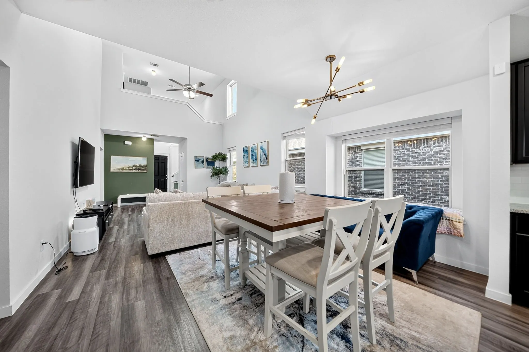 Open-concept dining and kitchen area featuring wood-finish flooring throughout, a dining table with seating for multiple guests, modern pendant lighting, and abundant natural light from large windows