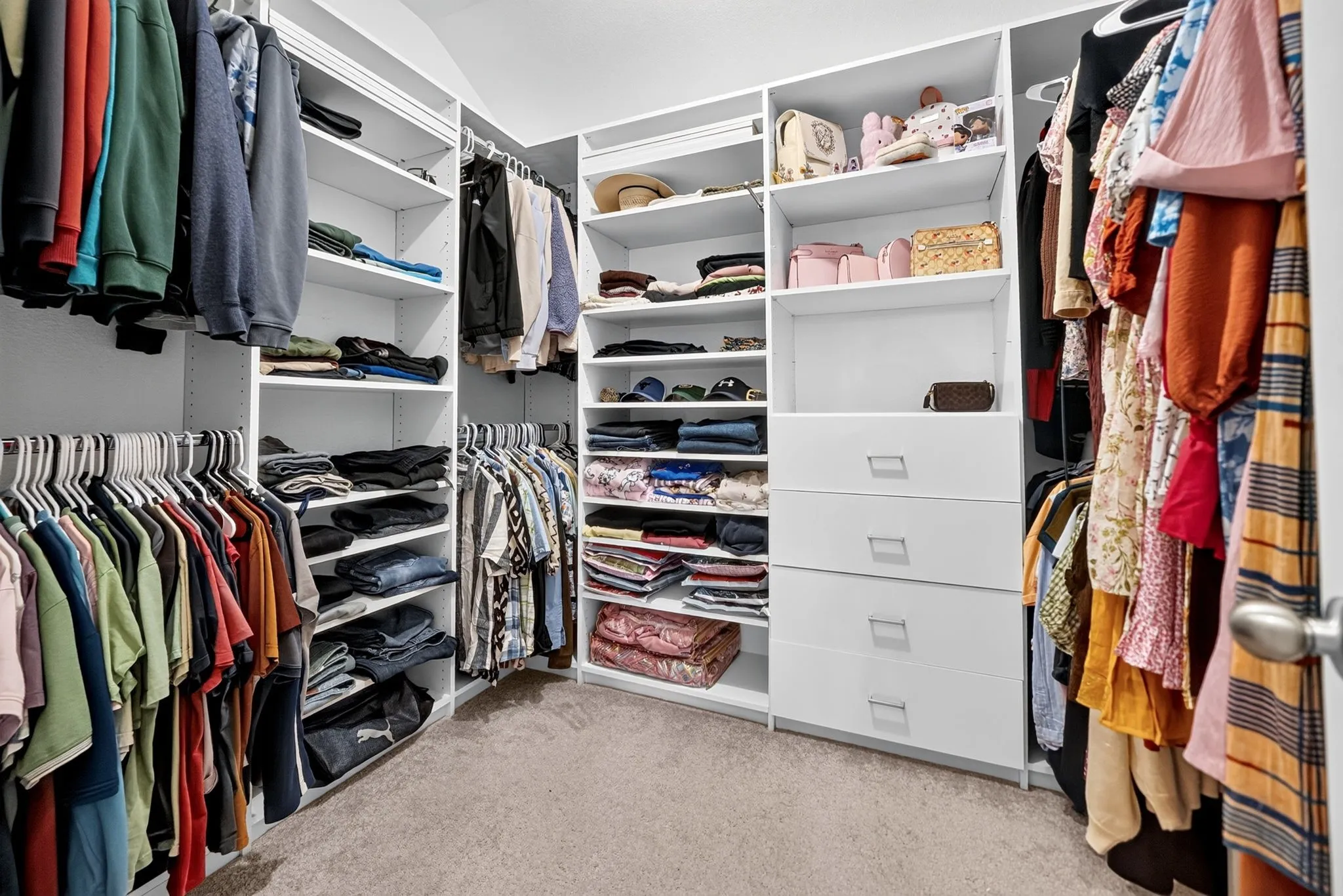 Built-in closet system featuring white shelving, multiple hanging rods, and integrated drawers