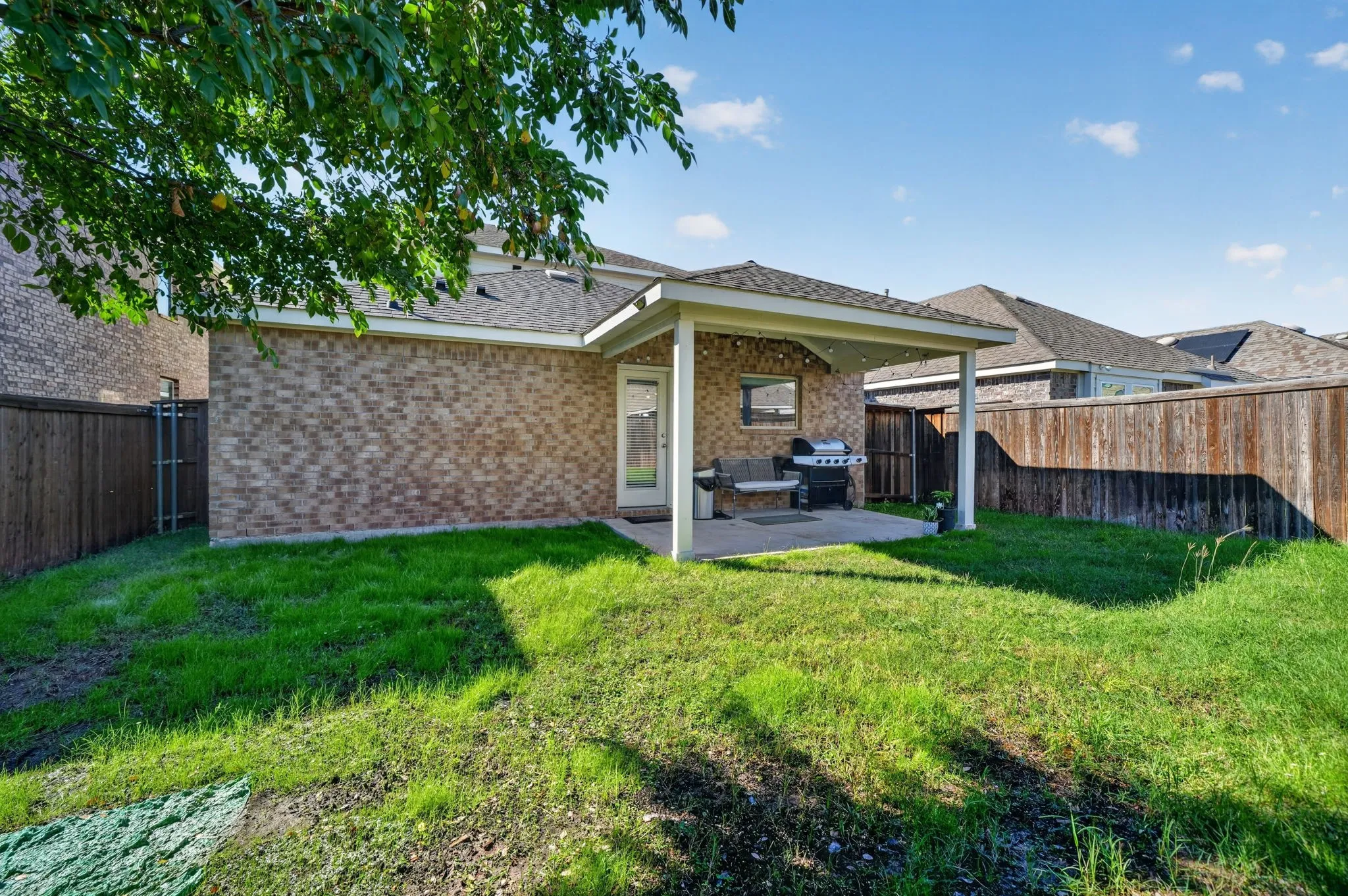 Private backyard with wood fencing, brick exterior, and a covered patio