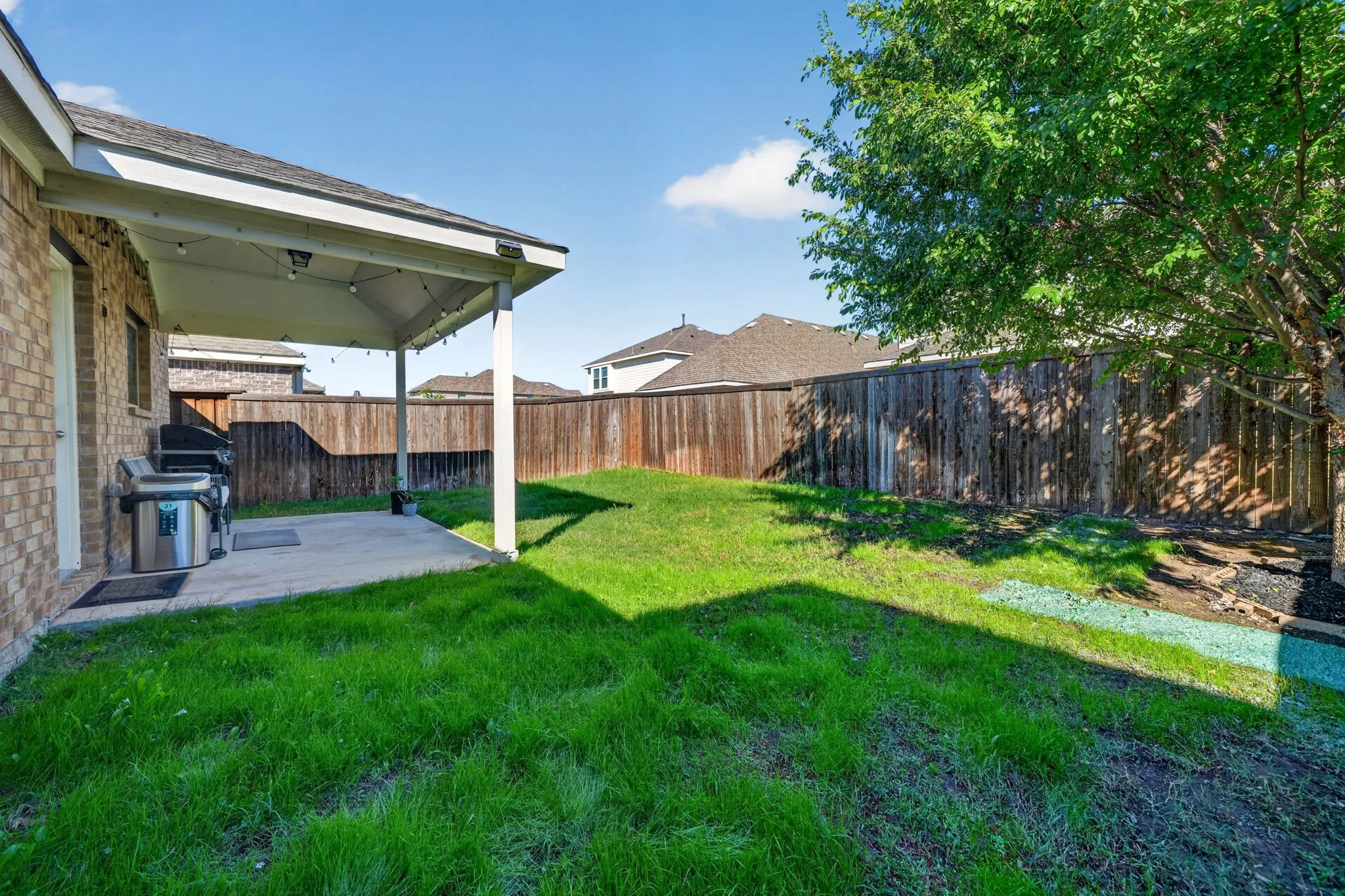 Covered patio with string lighting, concrete flooring, and a full privacy fence