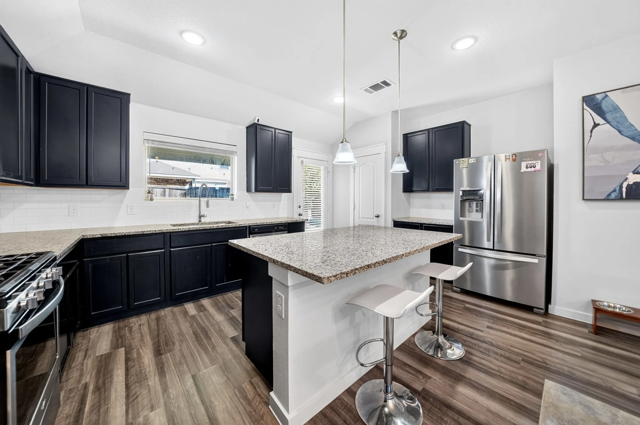 Kitchen featuring dark cabinetry, light countertops, wood-finish flooring, stainless steel appliances, and an island with pendant lighting