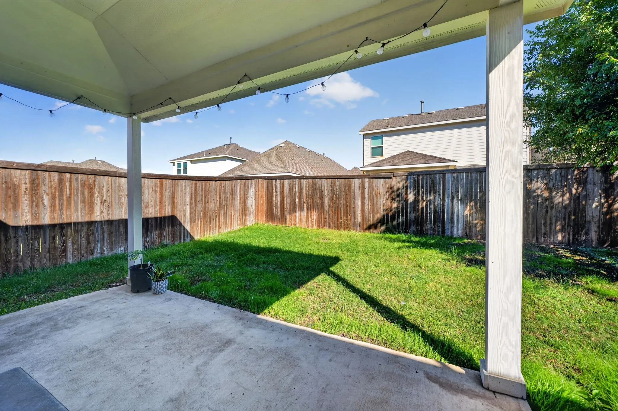 Covered patio with concrete flooring overlooking a spacious, level lawn bordered by wood-finish fencing
