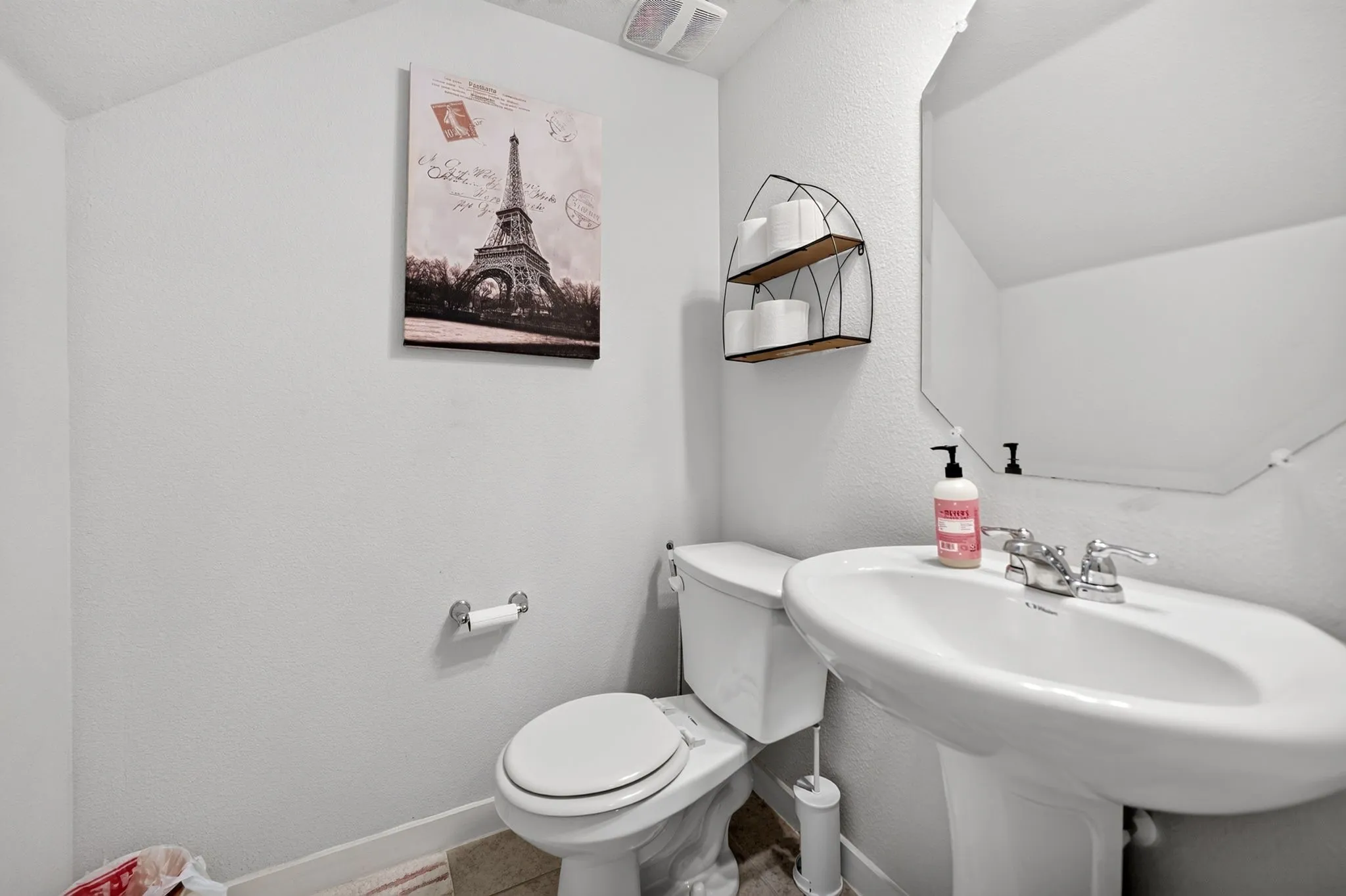 Pedestal sink with chrome faucet, toilet, wall-mounted mirror, and wall shelving
