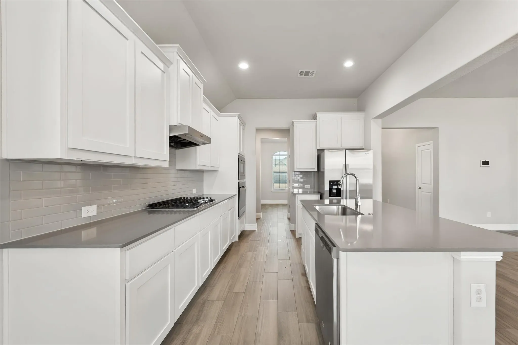 Modern kitchen featuring white cabinetry, gas cooktop, stainless steel appliances, quartz countertops, subway tile backsplash, and wood-finish flooring throughout the open layout with an island workspace