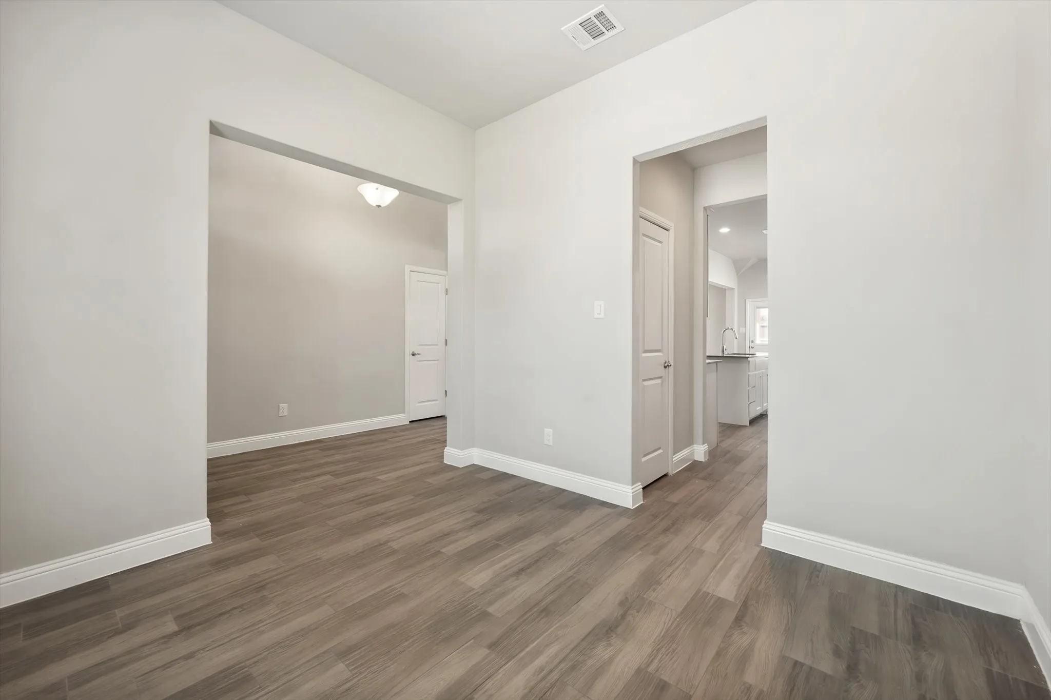 Spacious interior featuring pristine white walls, wood-look tile flooring throughout, and abundant natural light from recessed ceiling fixtures