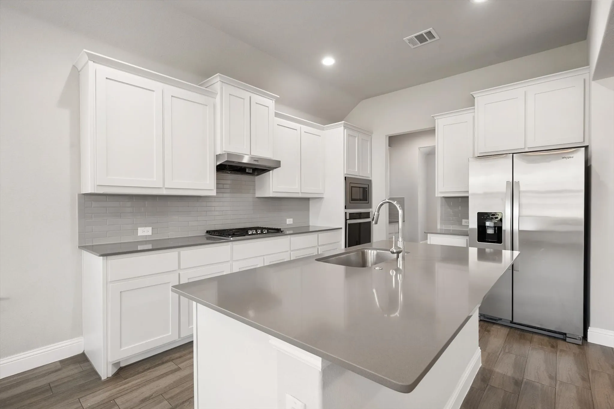 Contemporary kitchen featuring crisp white cabinetry, stainless steel appliances including a gas cooktop and built-in wall oven, quartz countertops, and a large island with extended seating