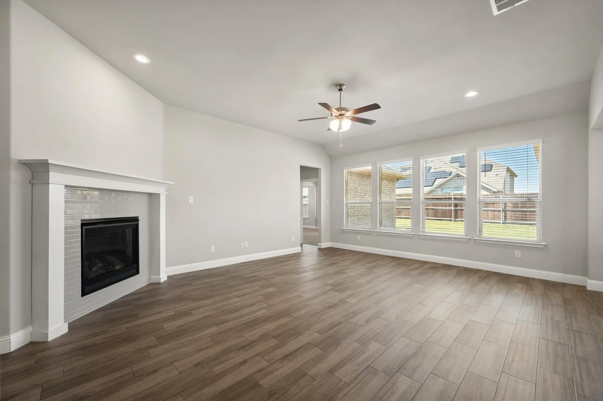 Spacious living room showcasing warm wood-finish flooring, recessed ceiling lighting, and a ceiling fan