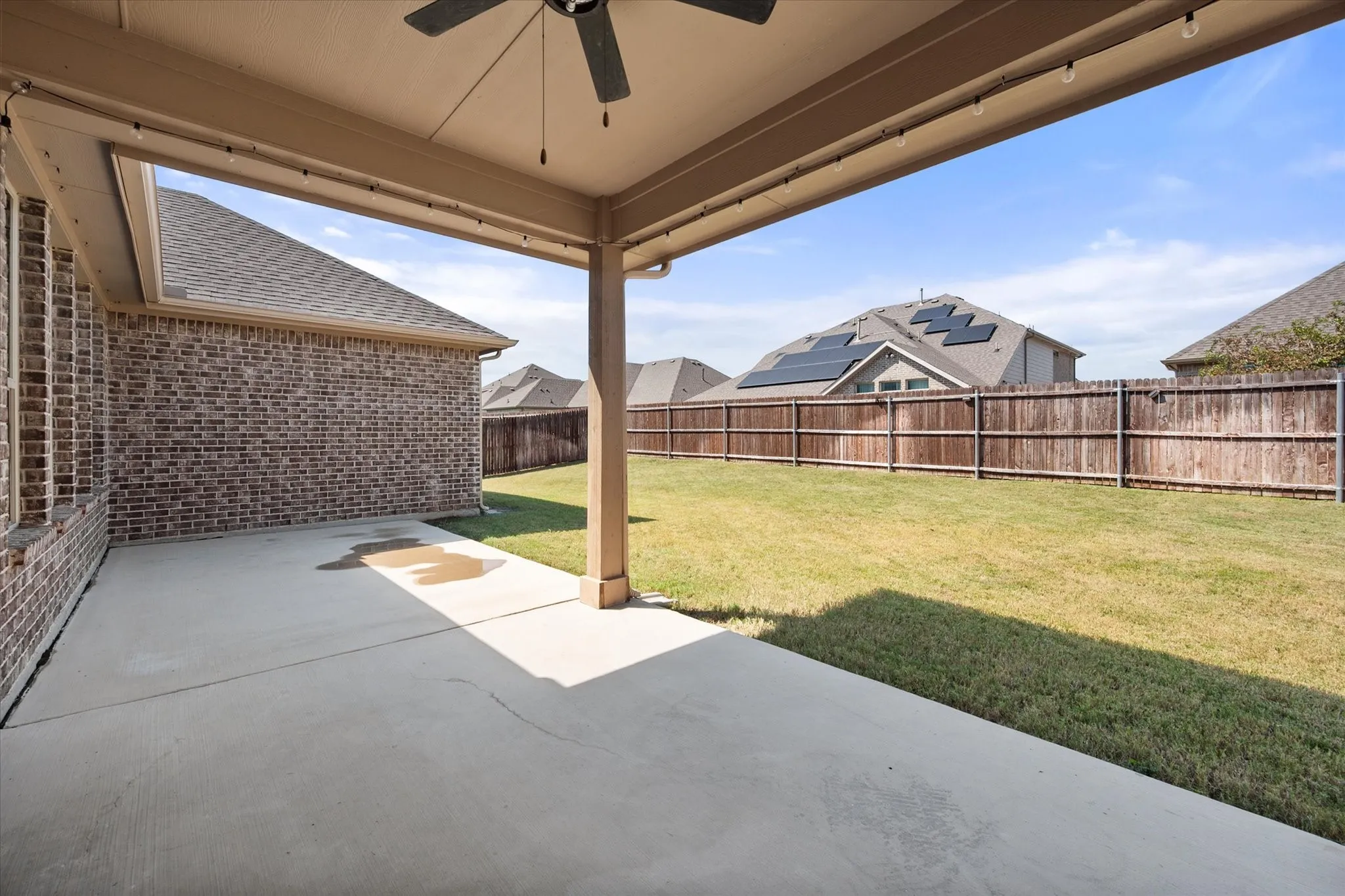 Covered patio with a ceiling fan, string lighting, and direct access to the expansive backyard featuring a wood fence and manicured lawn