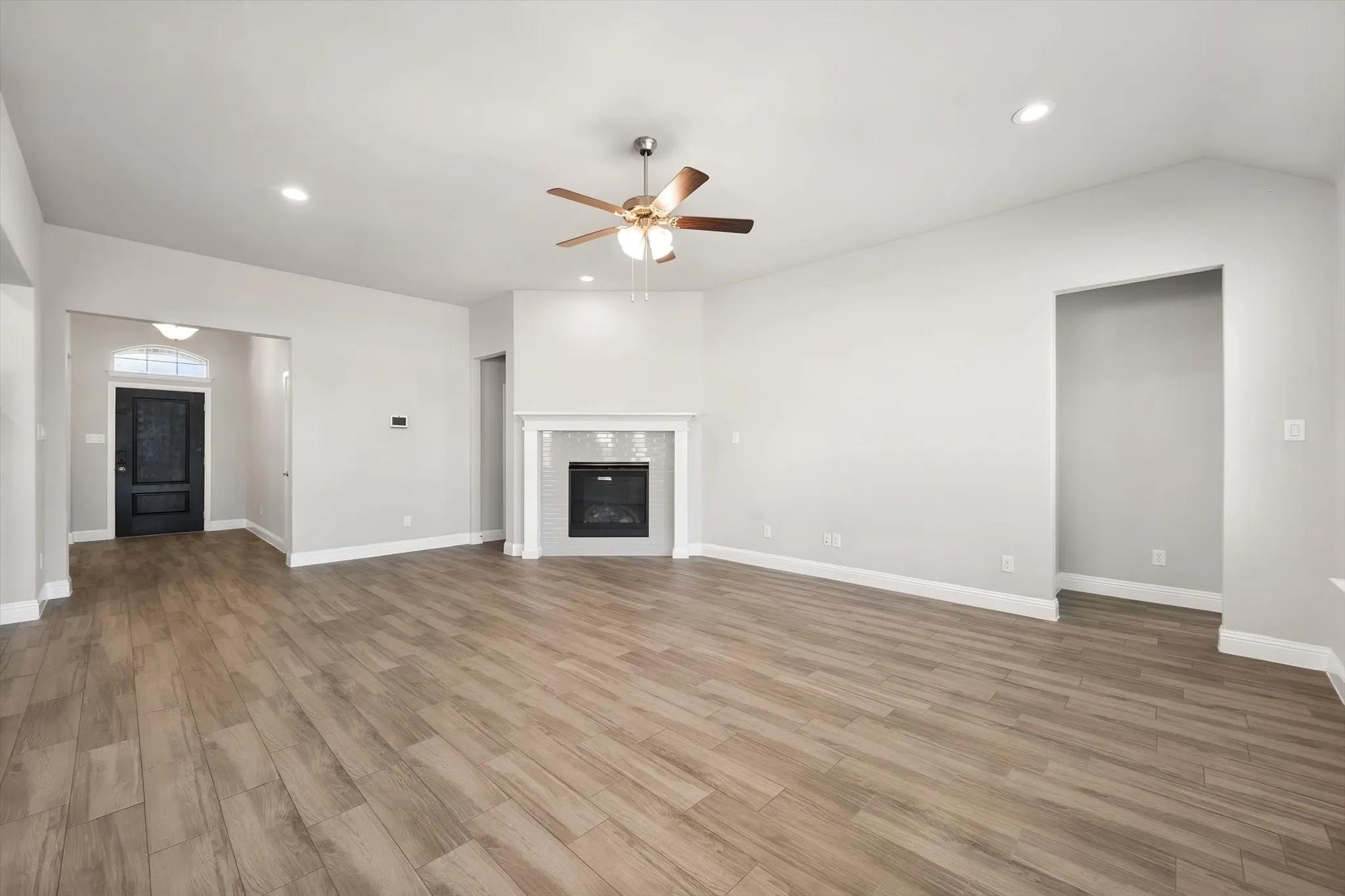 Spacious open-concept living area featuring wood-look tile flooring throughout, recessed ceiling lighting, and a ceiling fan with integrated light fixture
