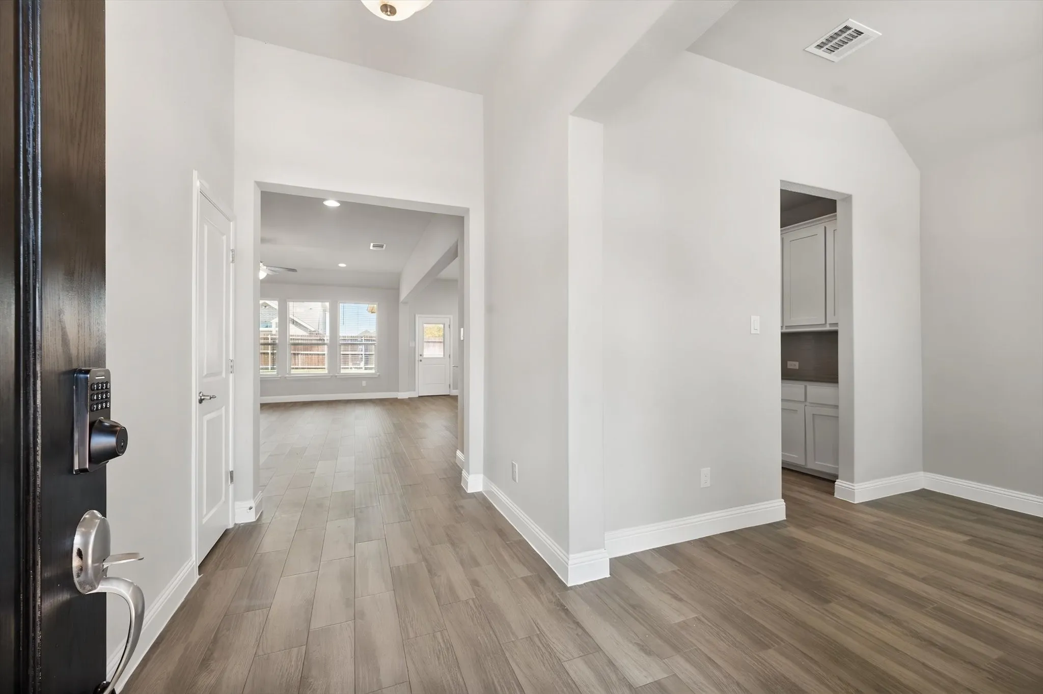 Woodlook tile flooring throughout, bright white trim, and a high vaulted ceiling in the entryway