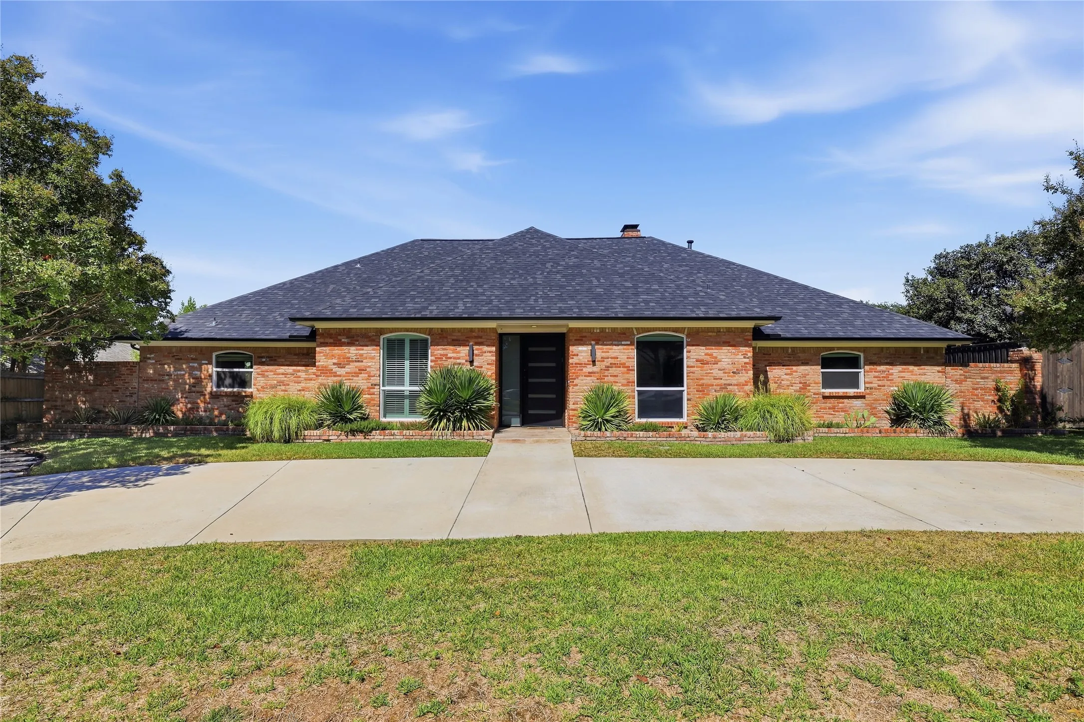 Brick-clad exterior with a dark shingle roof, arched window details, and mature landscaping