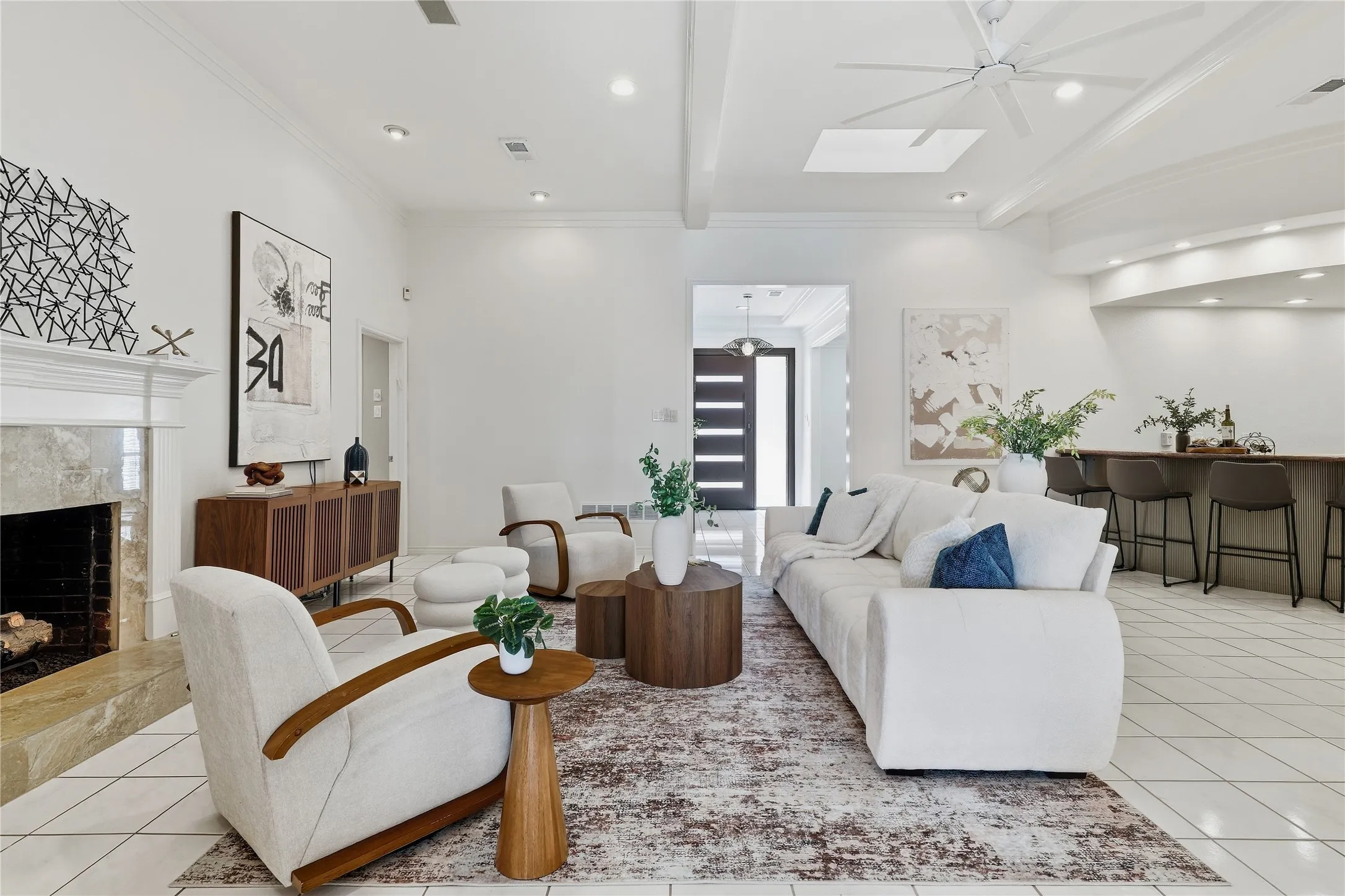 Spacious living area featuring a fireplace with a stone surround, tiled flooring, high ceilings with exposed beams, recessed lighting, and a built-in bar