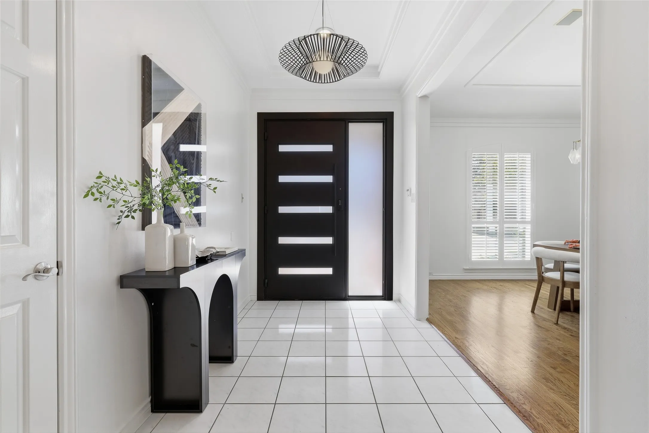 White square tile flooring, modern entryway pendant light, dark wood-finish entry door with frosted glass panels, white interior door, and light wood-finish flooring