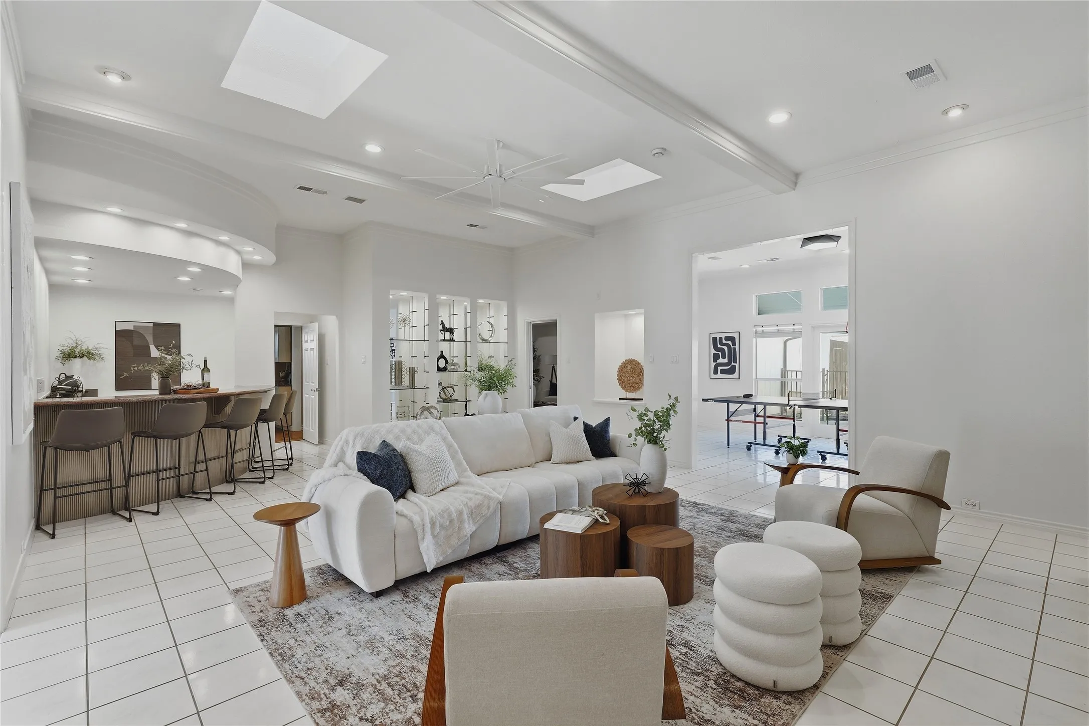 Spacious living area featuring white tile flooring, recessed lighting, and a built-in wet bar with a curved counter