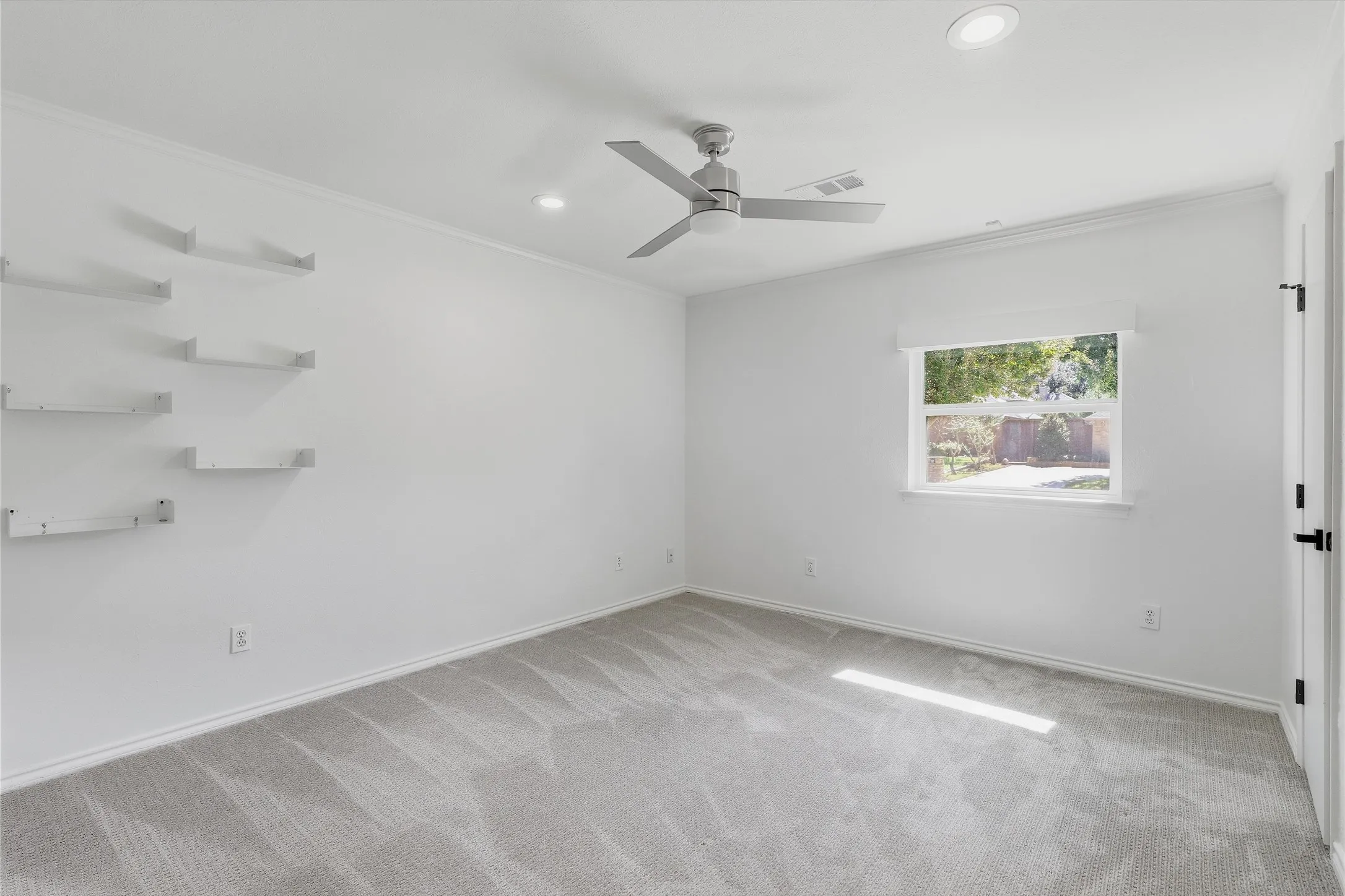 Recessed lighting, wall-mounted floating shelves, modern ceiling fan, and grey carpeting