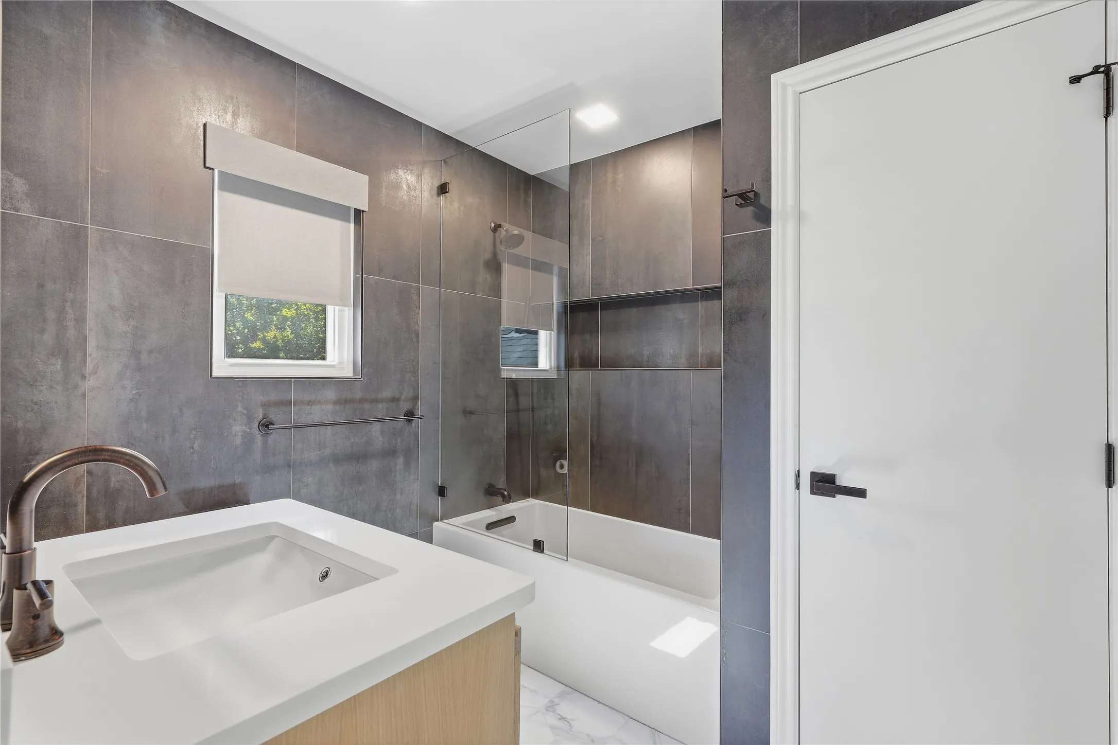 Modern bathroom featuring textured gray wall tiles, a white vanity with an integrated sink, and a bronze-finish faucet