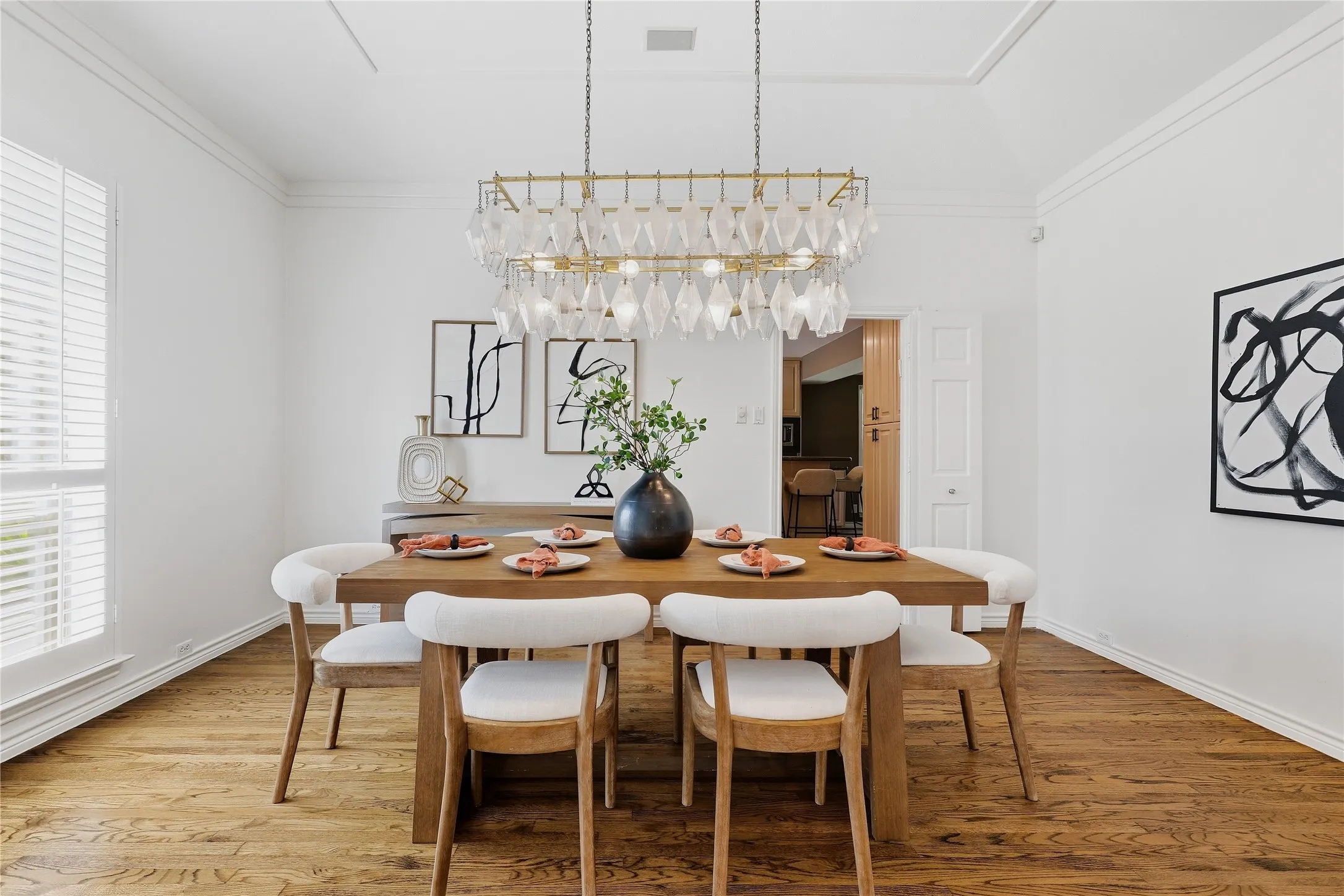 Hardwood flooring, crown molding, plantation shutters, vaulted ceiling, and a decorative chandelier