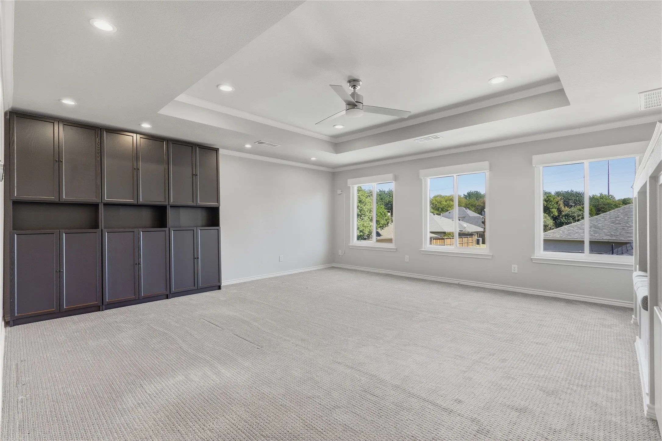 Recessed ceiling lighting, tray ceiling, ceiling fan, built-in cabinetry, and multiple windows