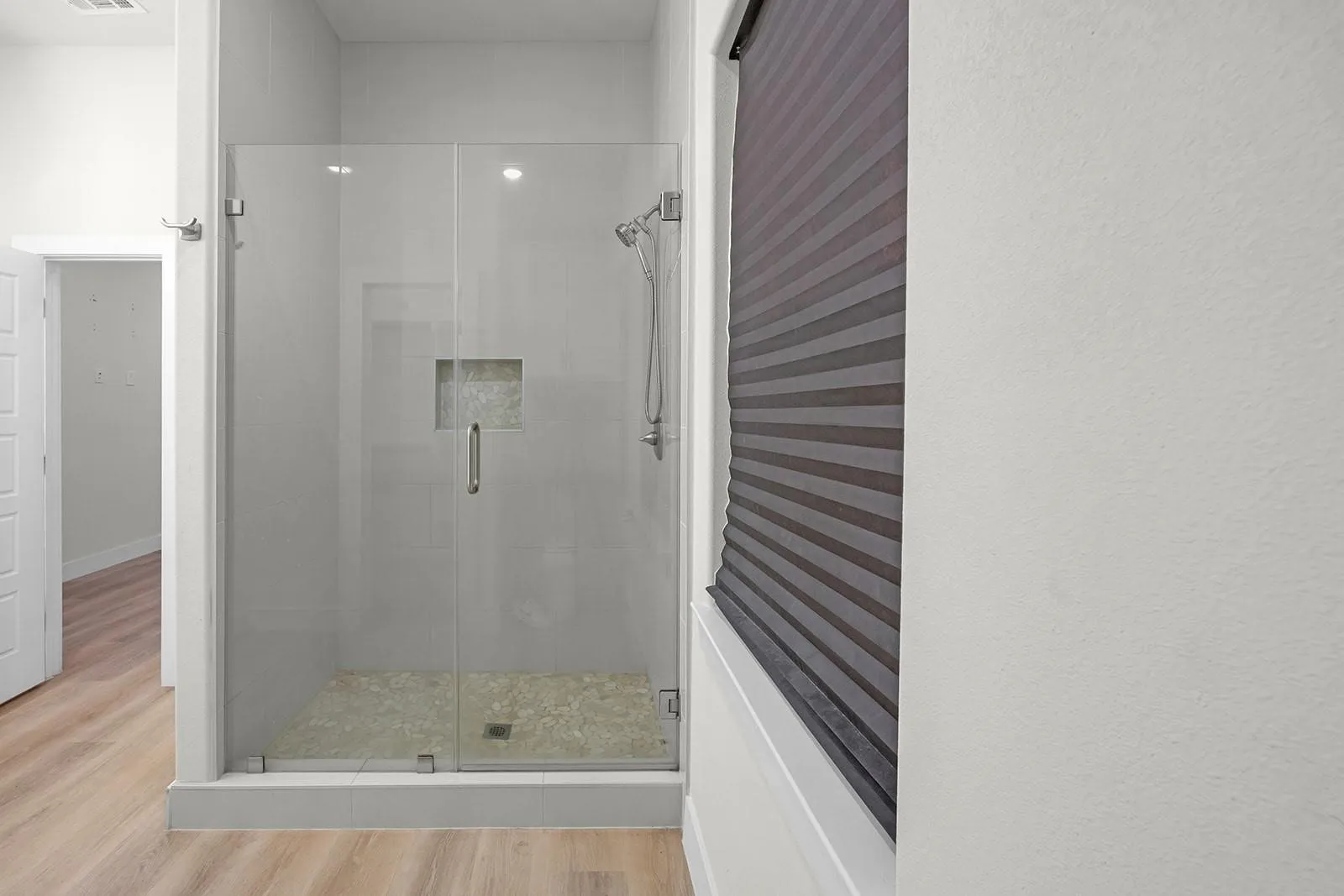 Spa-inspired ensuite featuring a frameless glass shower enclosure with brushed nickel hardware, pebble shower floor, and recessed niche shelving