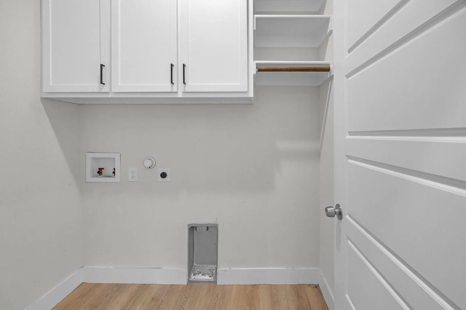 White upper cabinetry with black hardware, open shelving, wood-finish flooring, and a paneled door