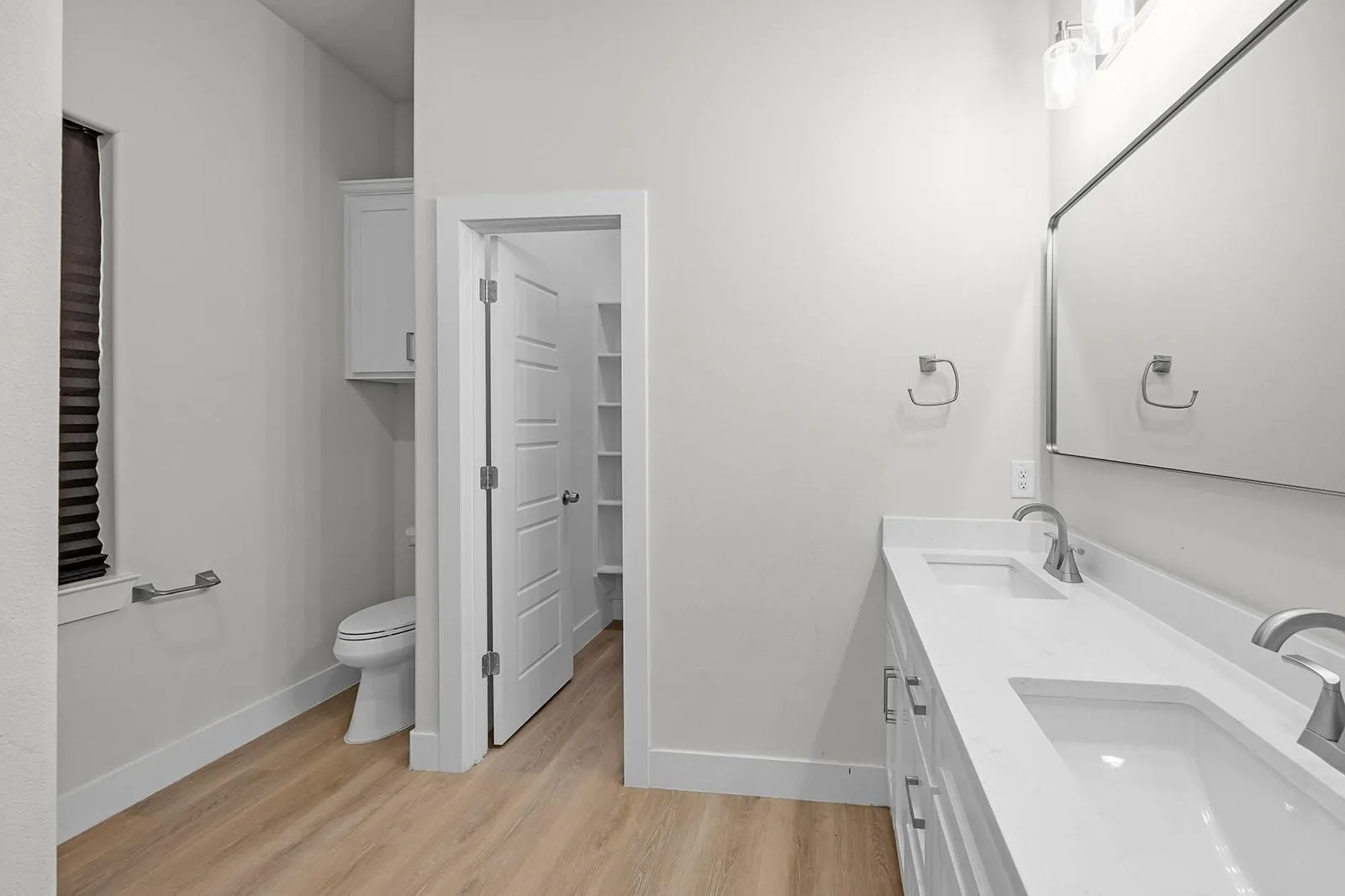 Double vanity with integrated sinks, wood-finish flooring, a wall-mounted medicine cabinet, and built-in shelving