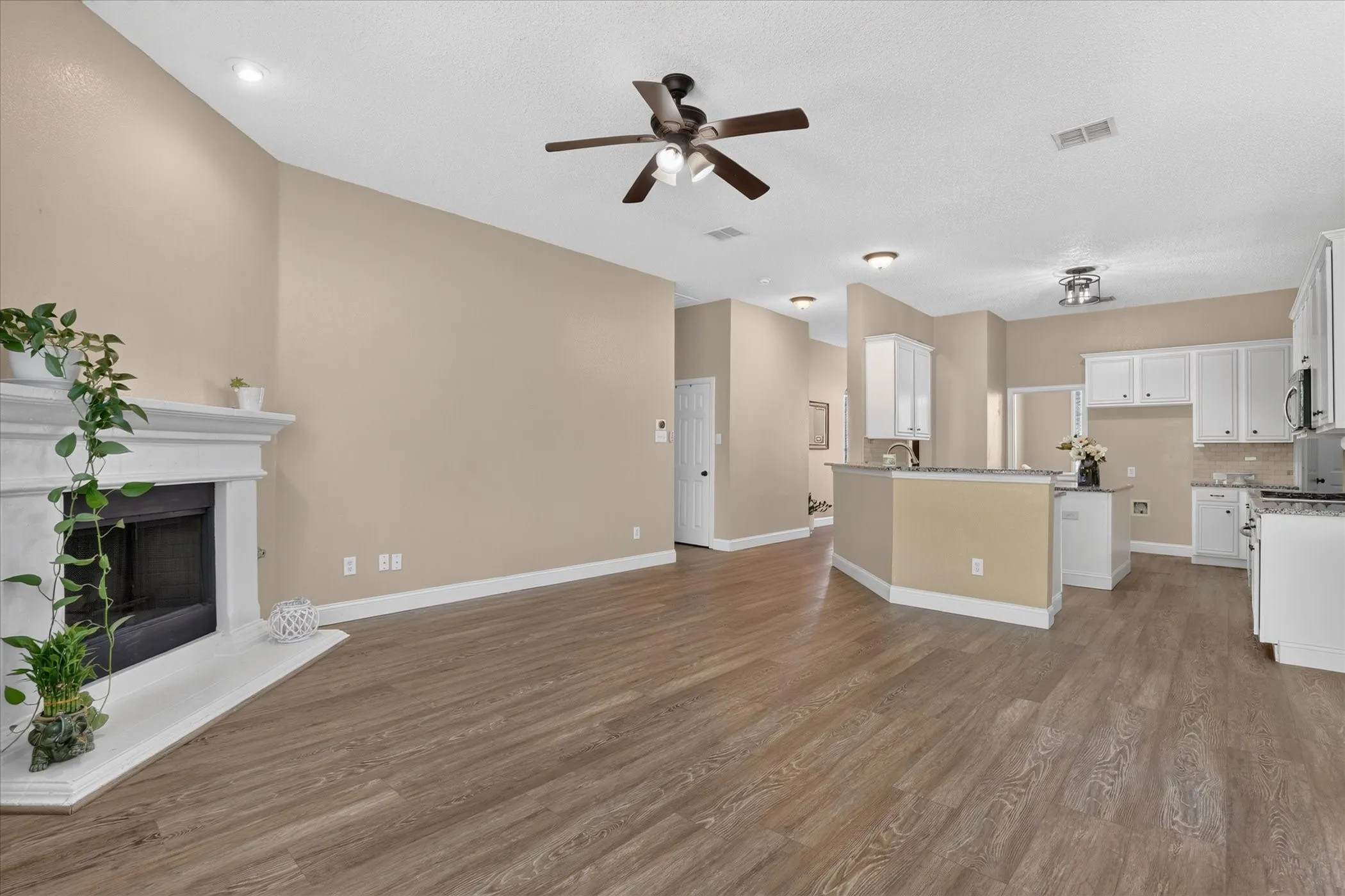 Open-concept living area with wood-finish flooring, a fireplace with a white mantel, and a ceiling fan