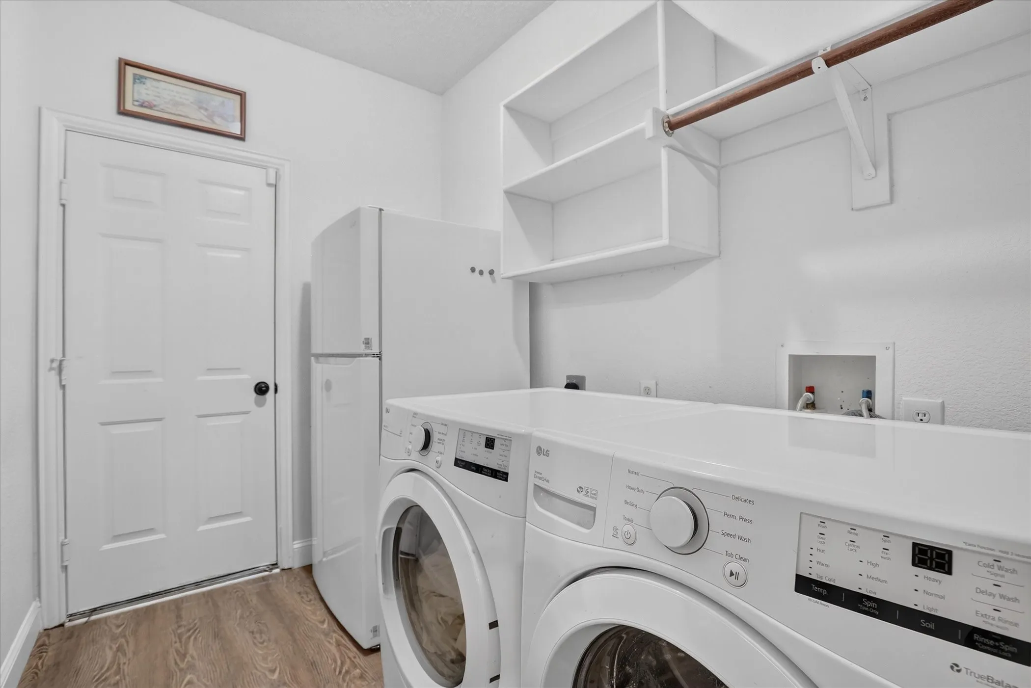 Dedicated laundry space featuring wood-finish flooring, white walls, built-in shelving, and a hanging rod