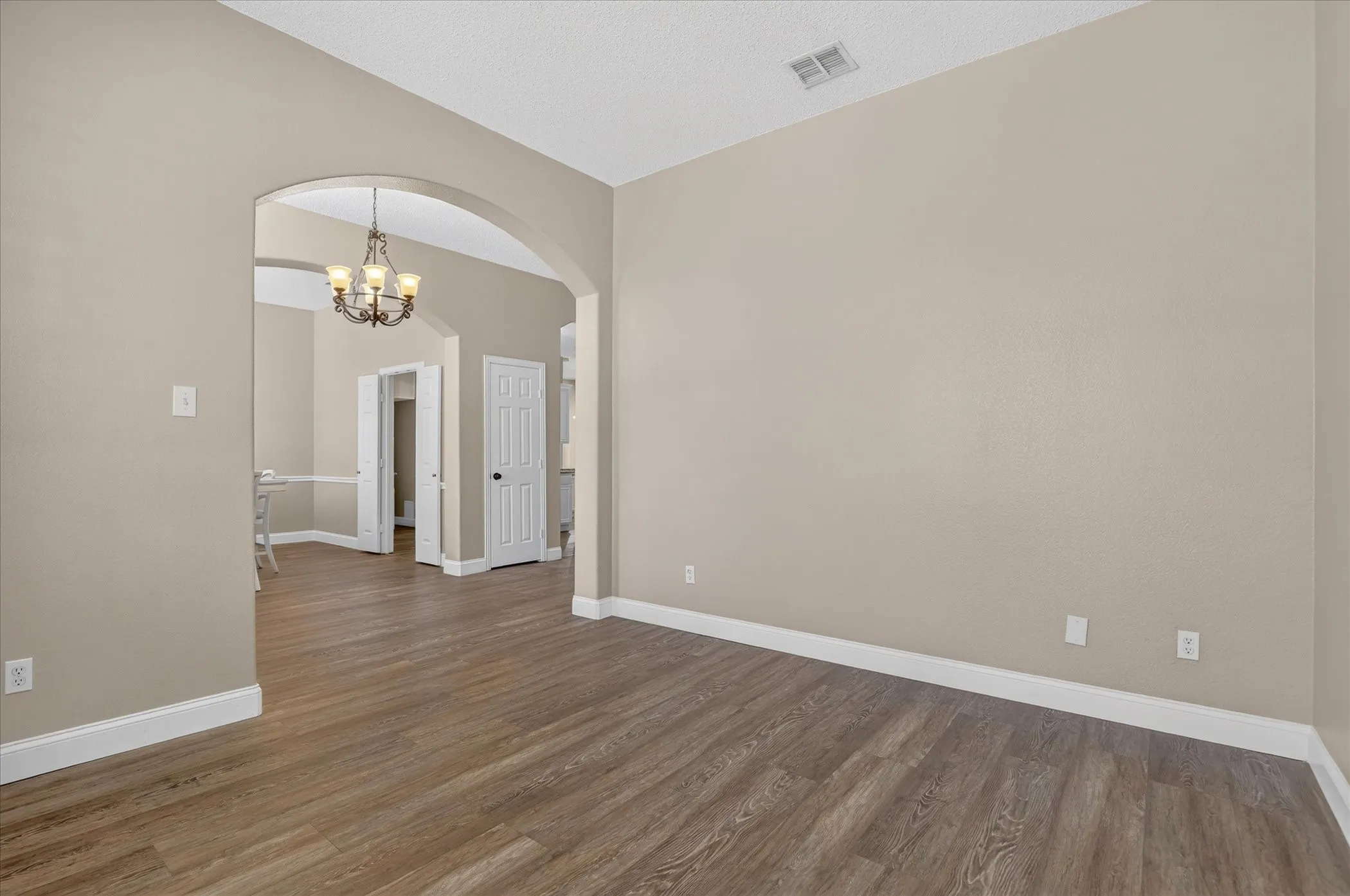 Archway entry with a chandelier, wood-finish flooring, and neutral wall paint