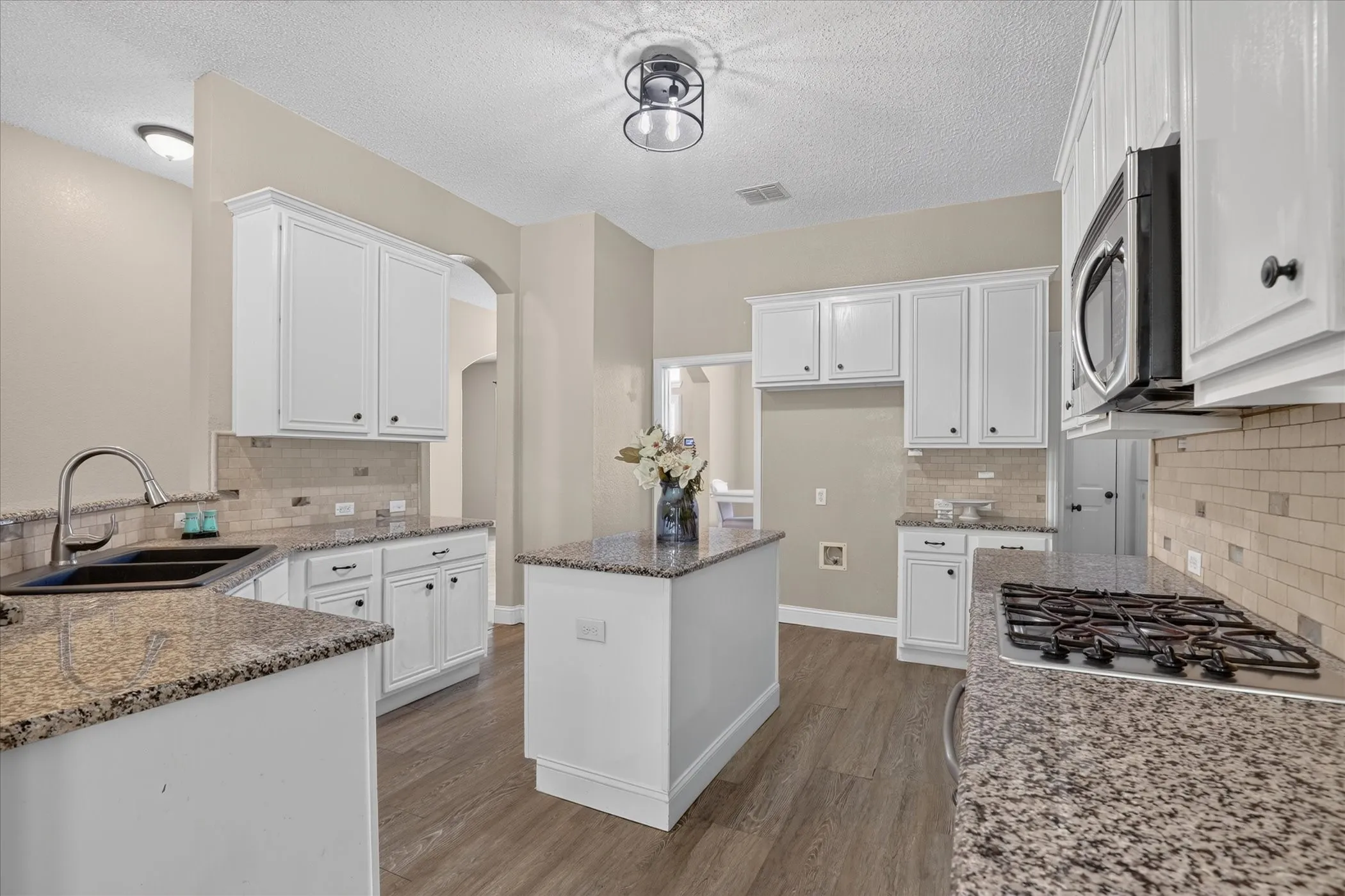 Kitchen featuring white cabinetry, granite countertops, tile backsplash, stainless steel appliances, and wood-finish flooring