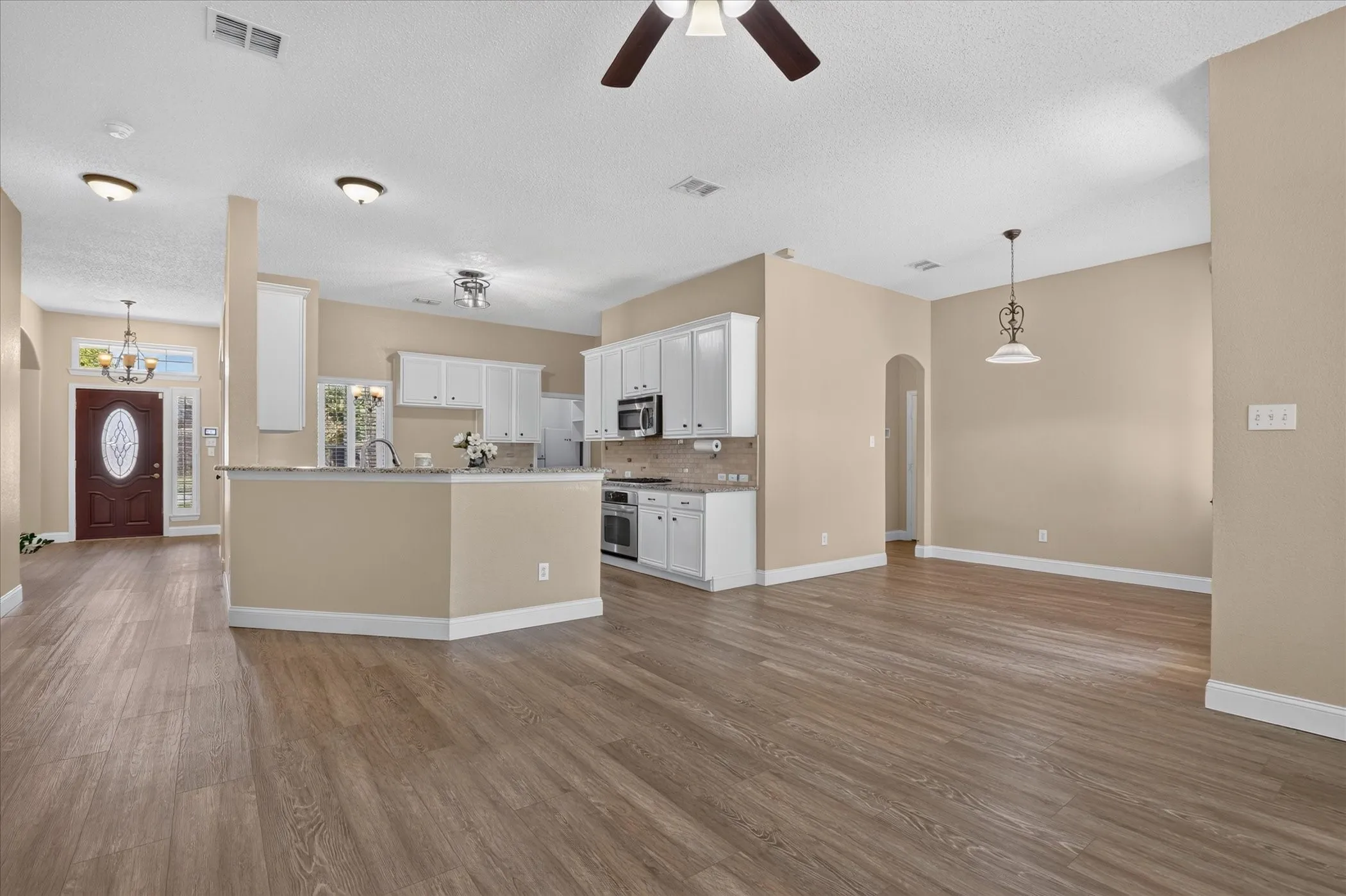 Open-concept living space with wood-finish flooring, white cabinetry, integrated stainless steel appliances, and a kitchen island with a stone countertop