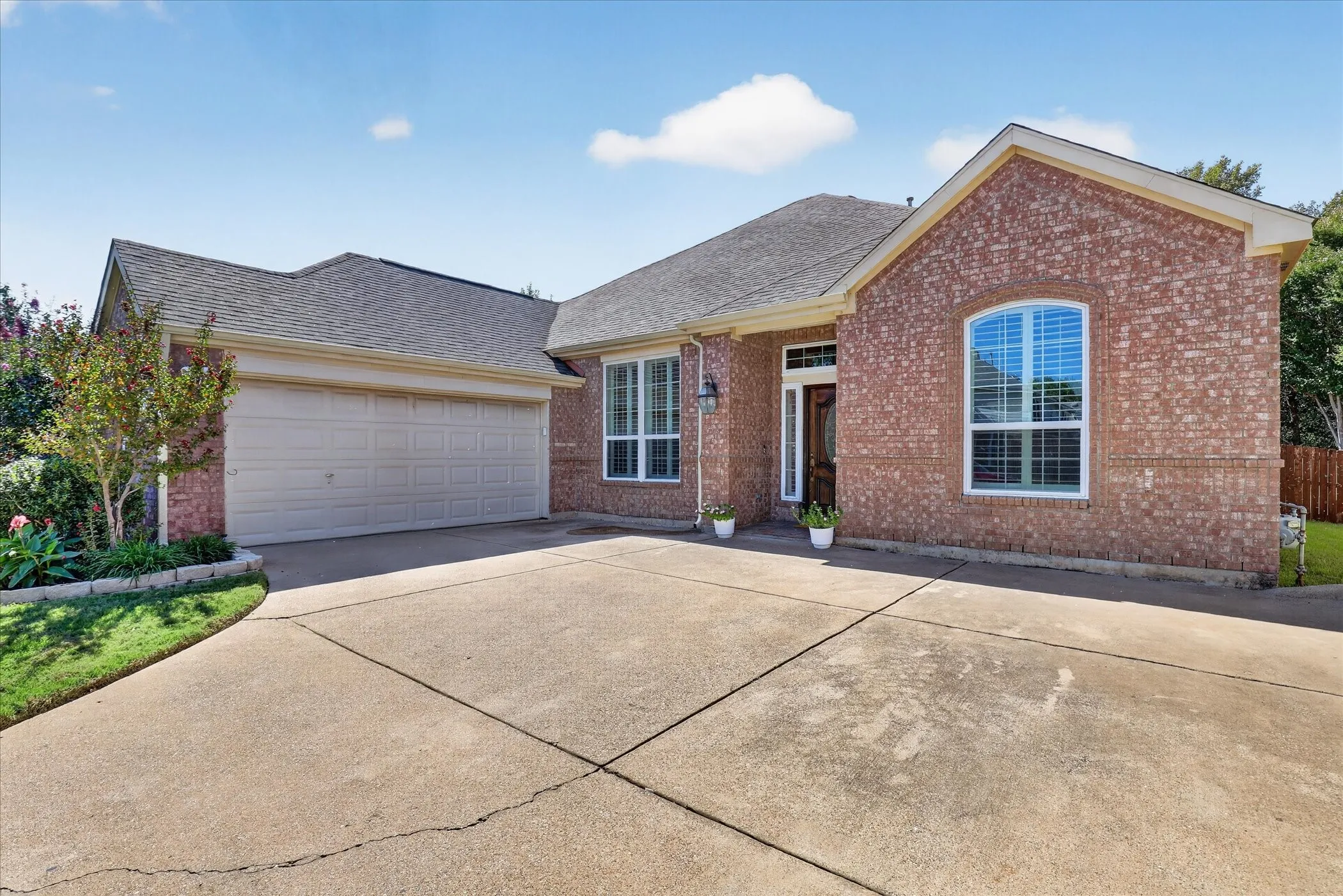 Brick exterior with arched window, concrete driveway, and attached garage