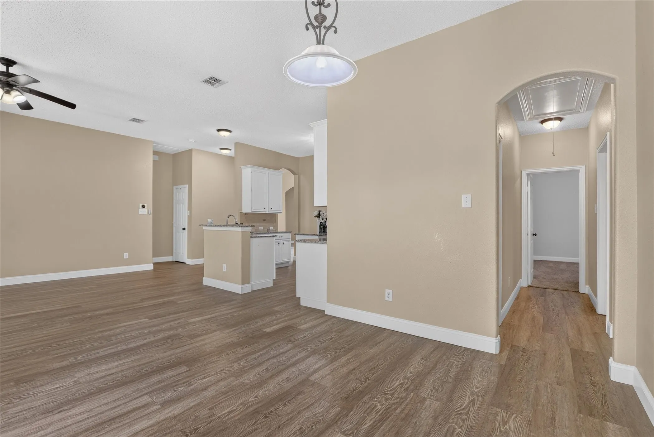 Wood-finish flooring throughout, ceiling fan, recessed lighting, white cabinetry, and an arched hallway entry