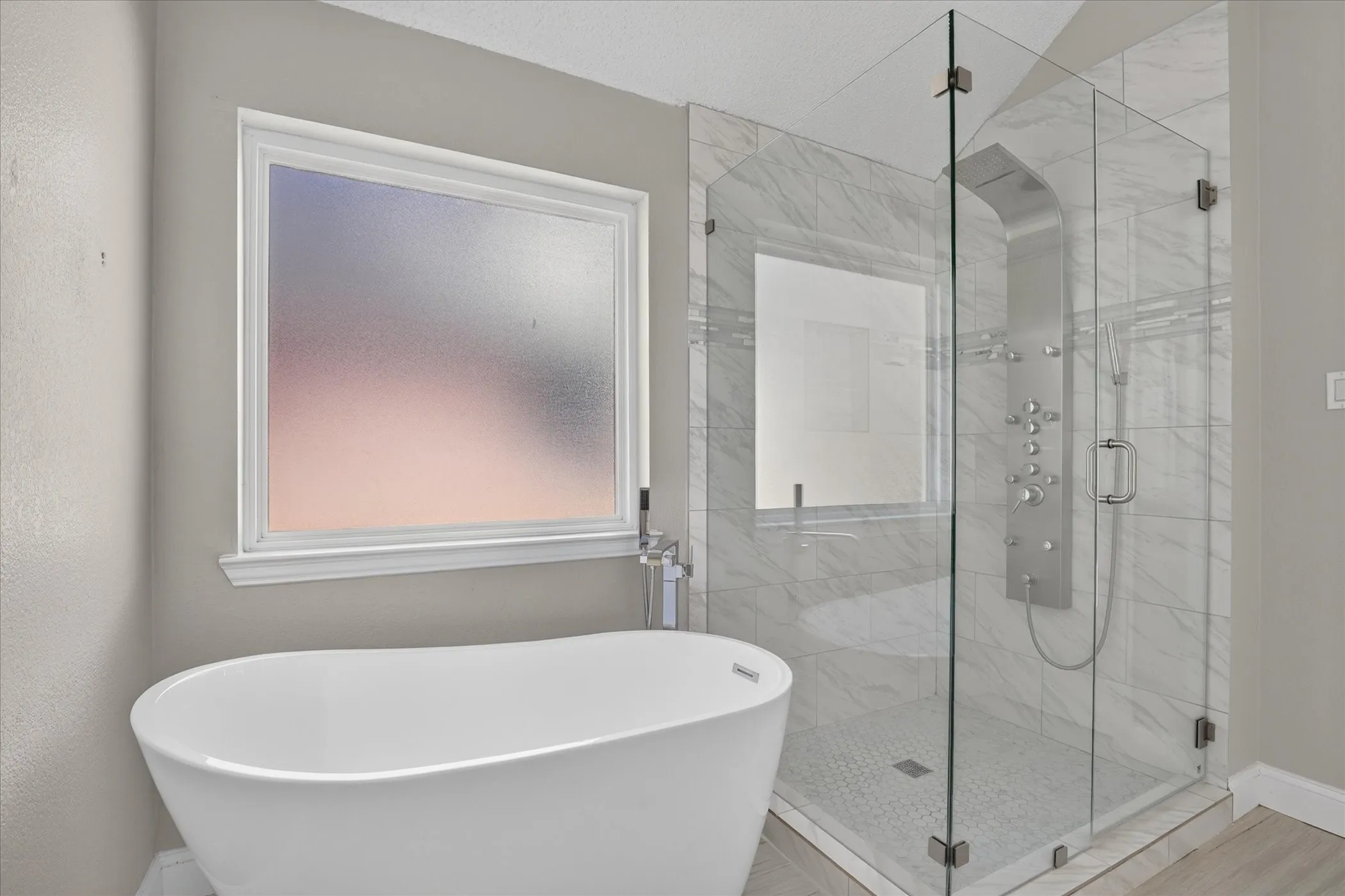 Freestanding soaking tub, frameless glass shower enclosure, multi-function shower panel, white tile surround, and frosted window
