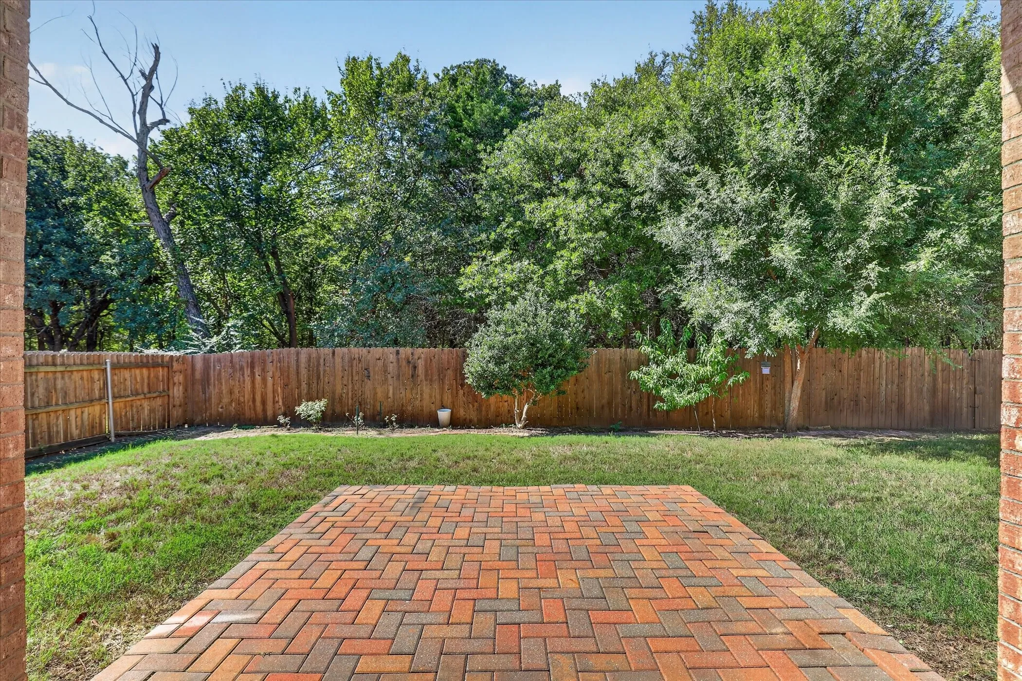 Brick patio with a herringbone pattern, wood privacy fence, and mature trees