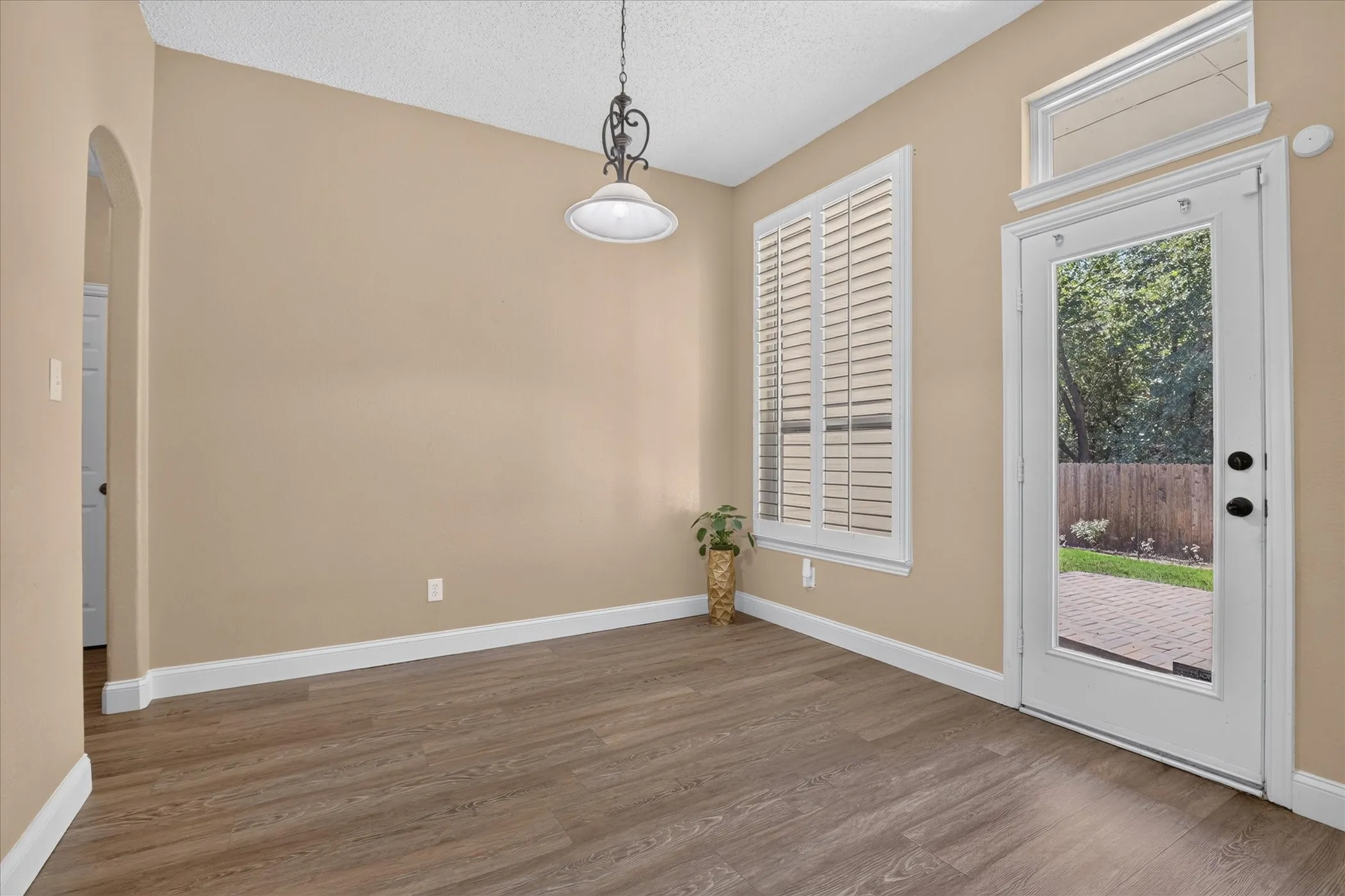 Wood-finish flooring, arched entryway, and a white plantation-shutter window