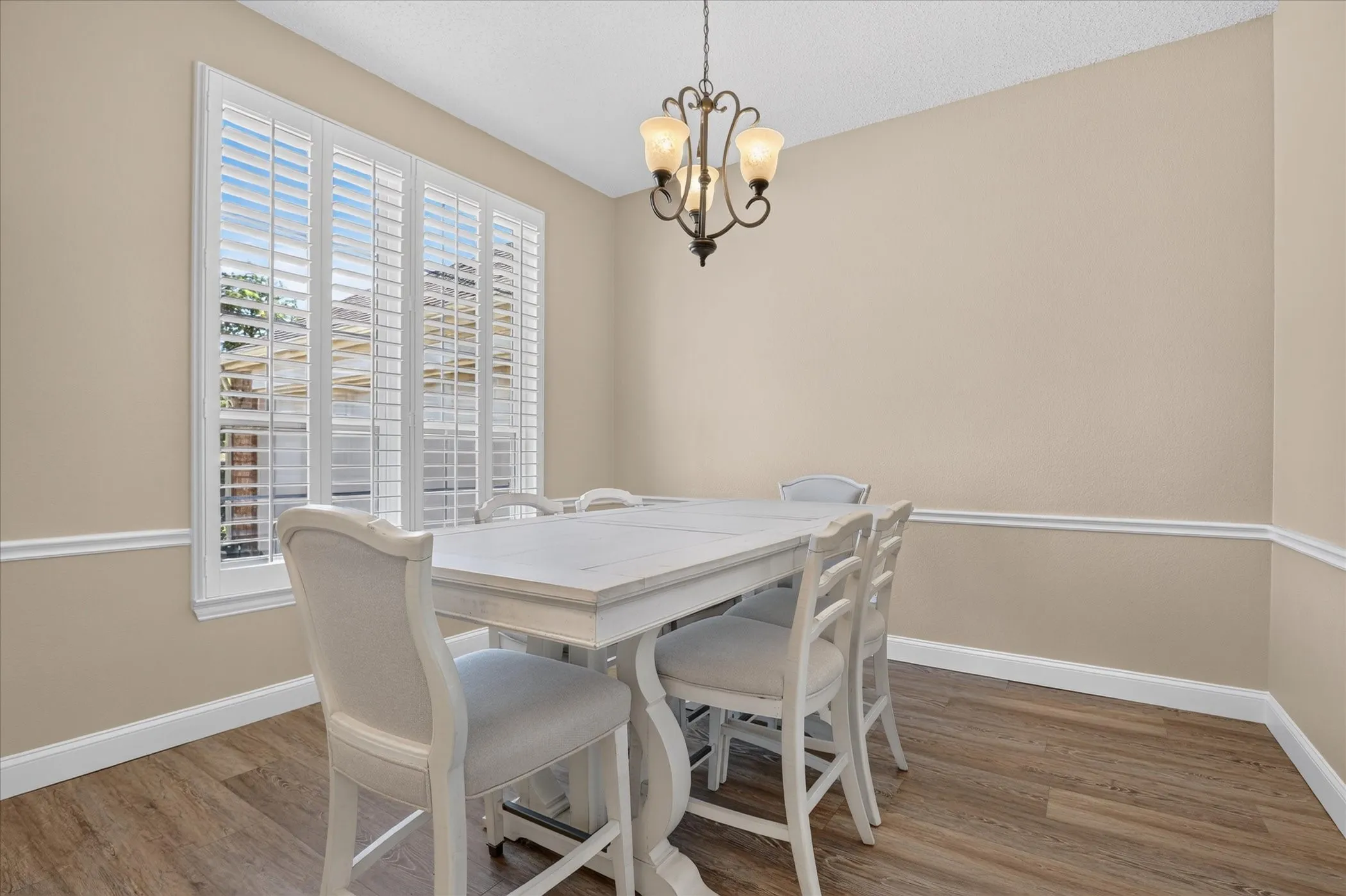 Wood-finish flooring, white window shutters, decorative chair rail molding, and an overhead chandelier