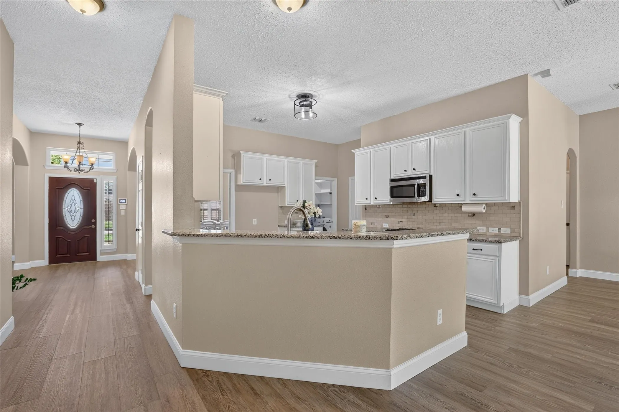 Kitchen featuring white cabinetry, stainless steel microwave, stone countertops, and tile backsplash