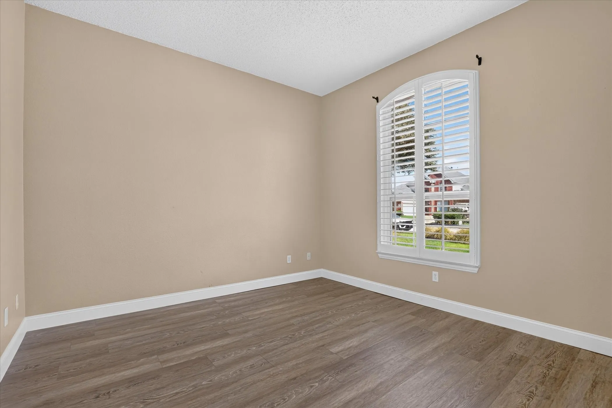 Arched window with plantation shutters, wood-finish flooring, and neutral wall tones