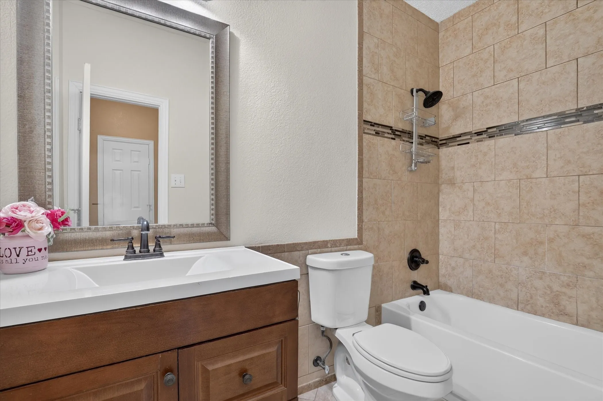 Bathroom featuring a wood-finish vanity with an integrated sink, framed mirror, and a bathtub with tiled surround