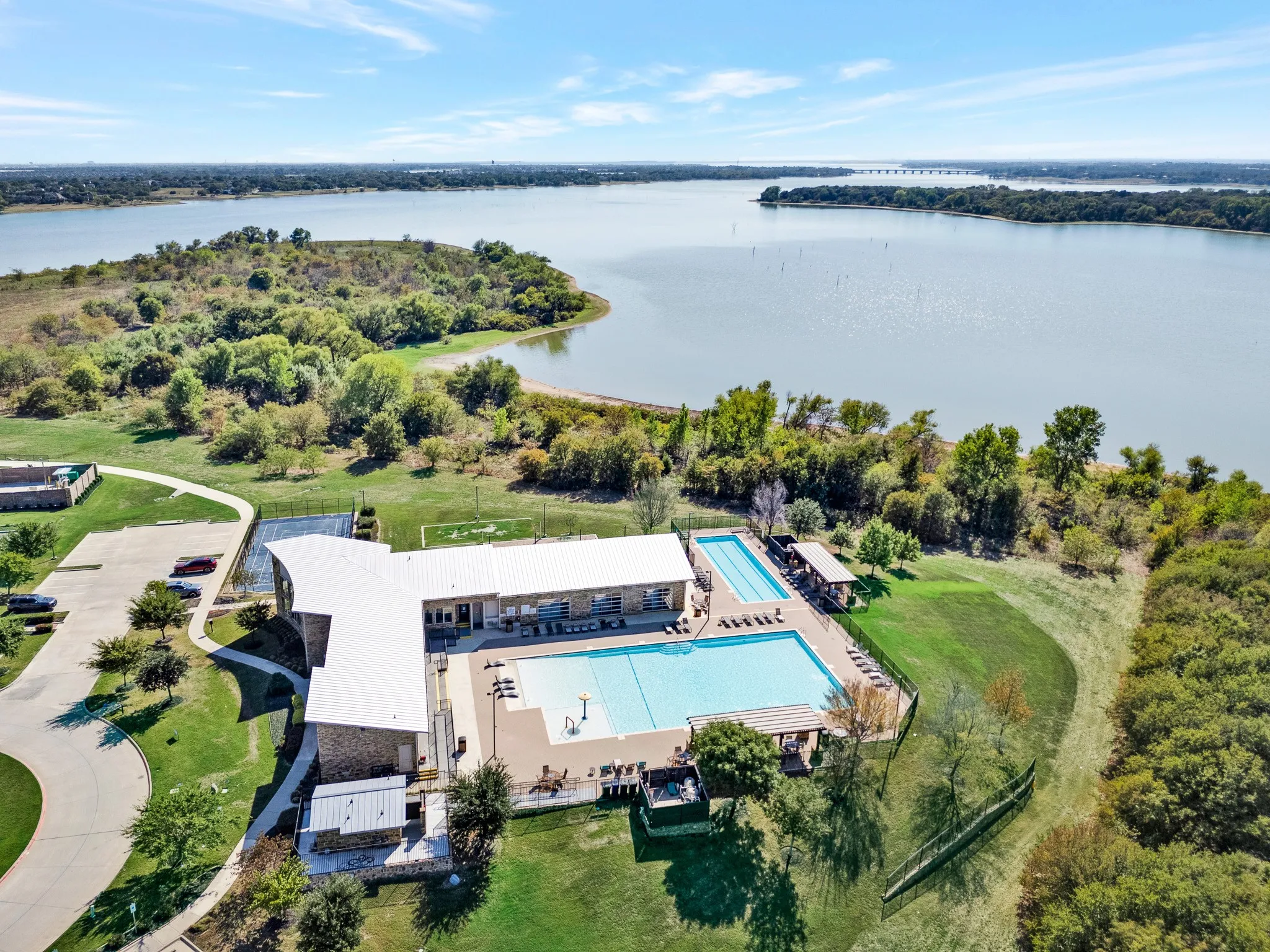 Expansive lakefront property featuring a community building, two outdoor swimming pools, tennis court, and manicured green space