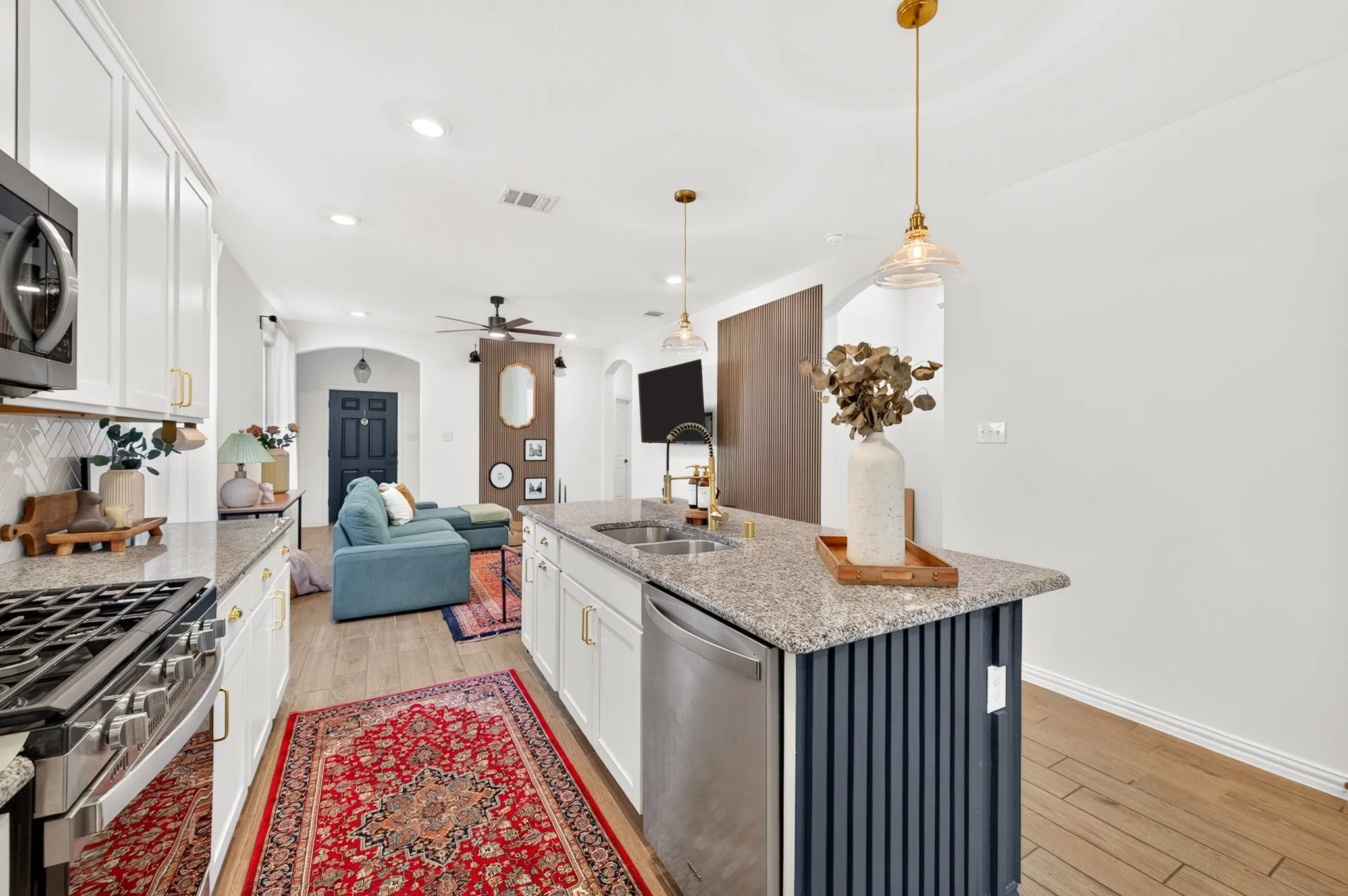 Kitchen featuring a gas range, stainless steel dishwasher, white shaker cabinetry, and an island with a built-in sink and granite countertop