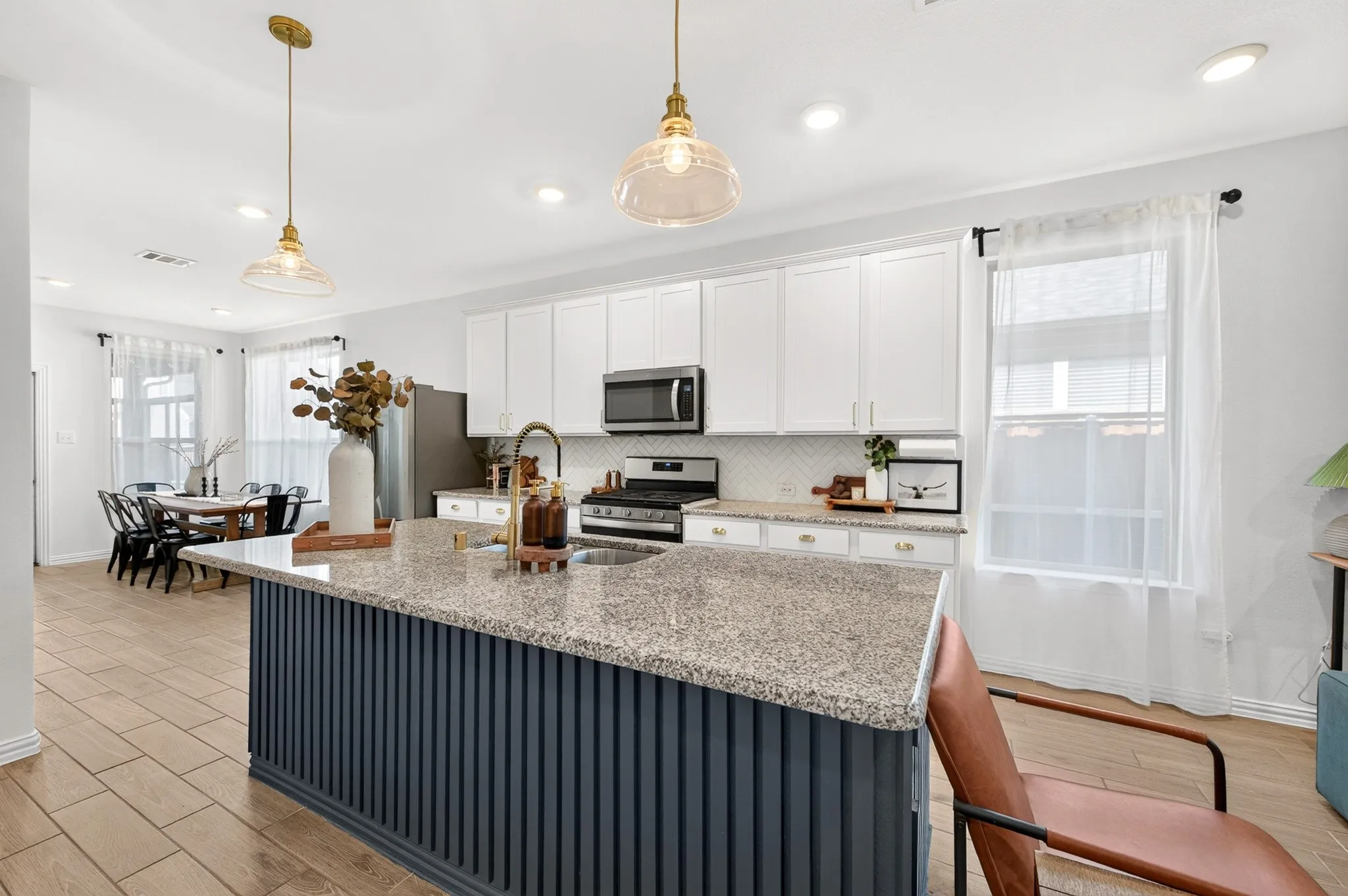 Kitchen featuring a granite-top island with fluted paneling, stainless steel appliances, white cabinetry with brass hardware, and wood-finish flooring