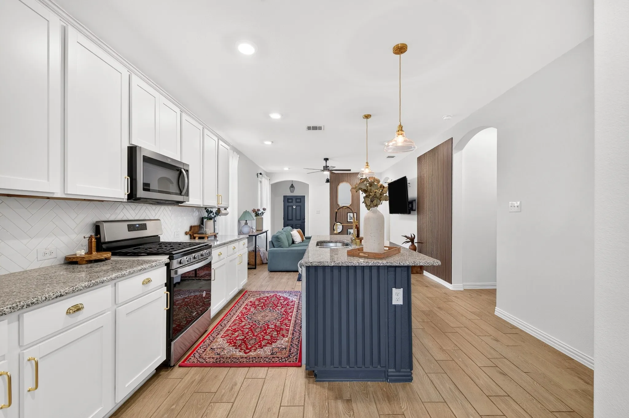 White cabinetry, stainless steel appliances, granite countertops, wood-finish flooring, and an arched entryway
