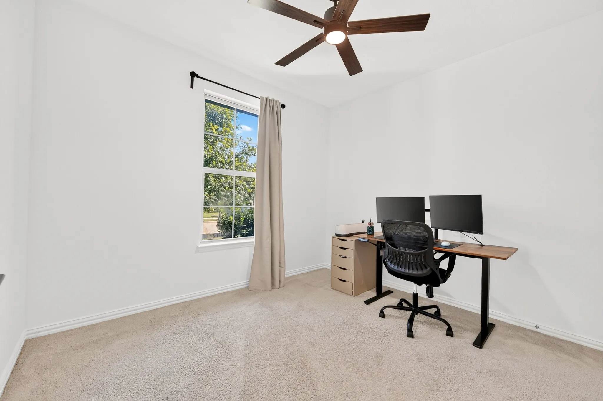 Carpeted flooring, white walls, window with black curtain rod, and ceiling fan with light fixture