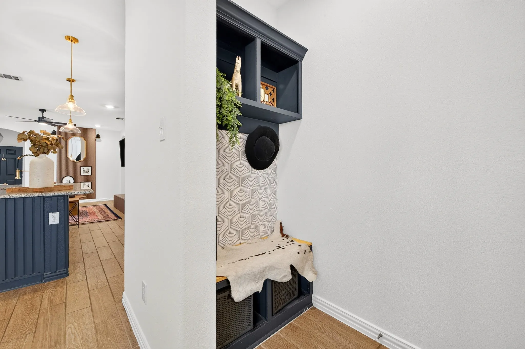 Dedicated mudroom entry featuring built-in black cabinetry with lower storage cubbies, floating shelf display with integrated black speaker, and wood-finish flooring that extends seamlessly from the adjacent kitchen