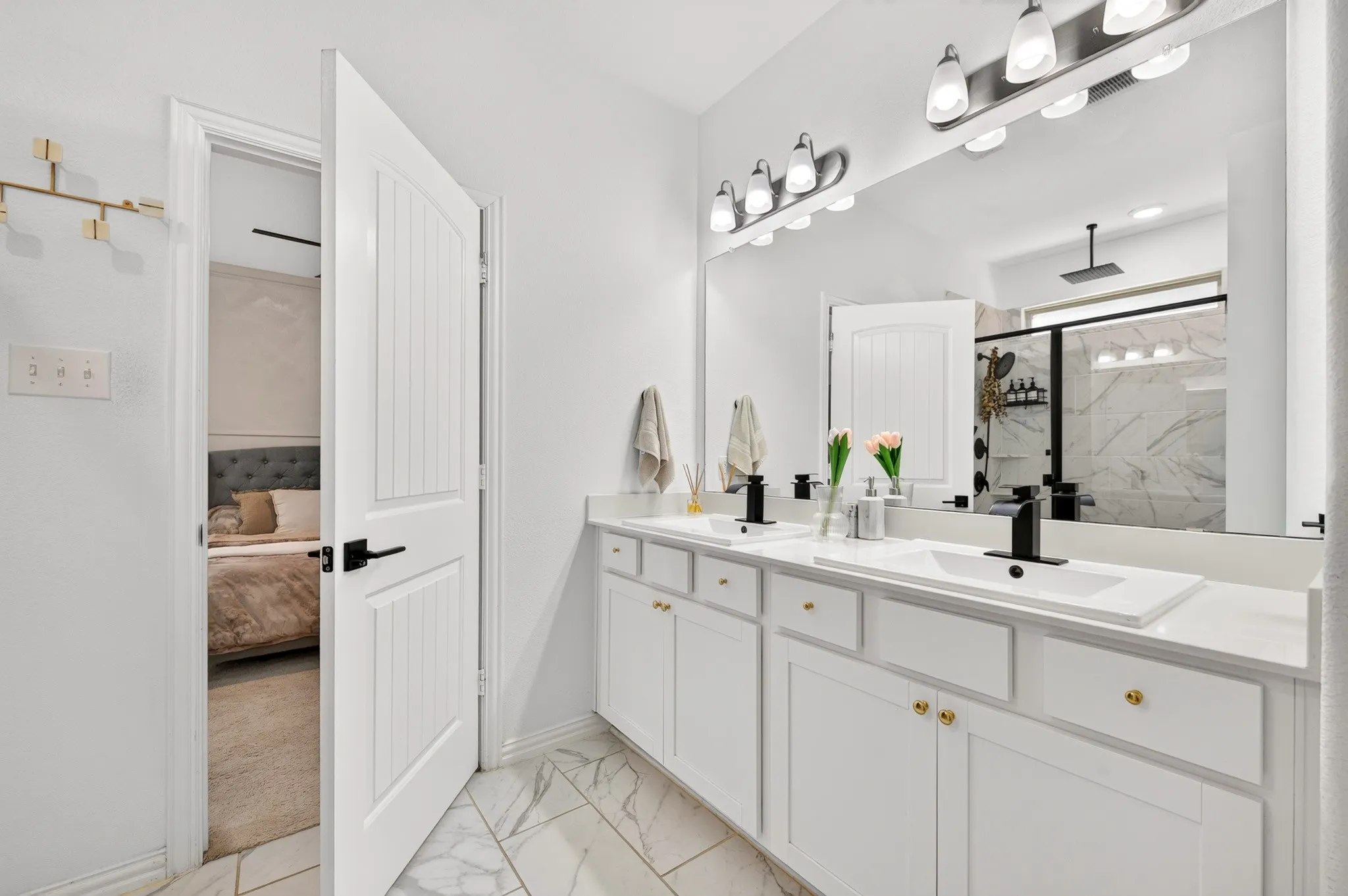 Spa-inspired primary bathroom featuring dual vanities with white cabinetry, white quartz countertops, and brushed gold hardware