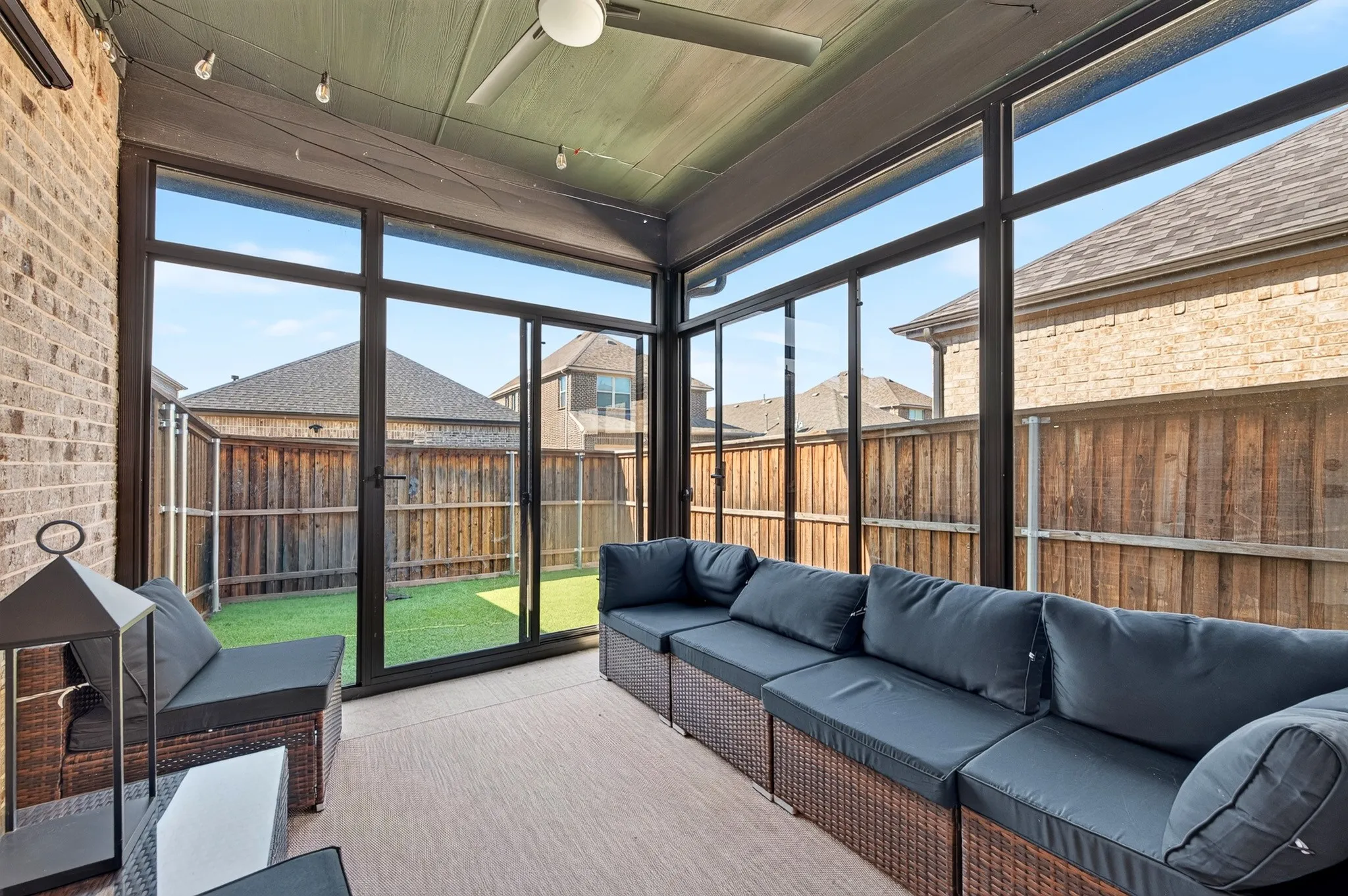 Enclosed sunroom featuring floor-to-ceiling black-framed glass panels, composite decking, and a coffered ceiling with recessed lighting