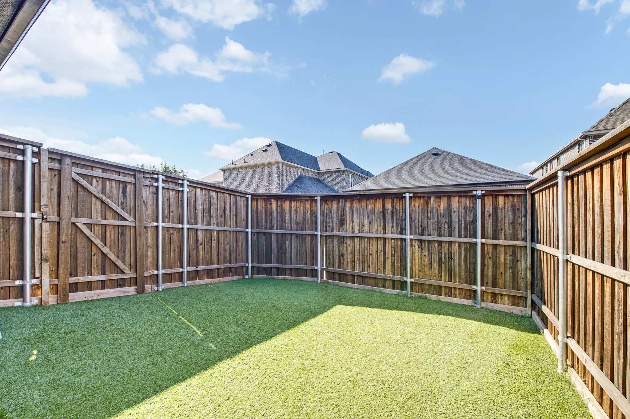 Enclosed backyard featuring artificial turf, tall wood privacy fencing, and a wooden gate