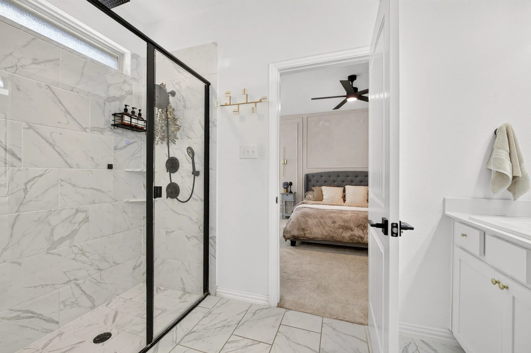 Walk-in shower with black-framed glass enclosure, marble-style tile walls, and a recessed window