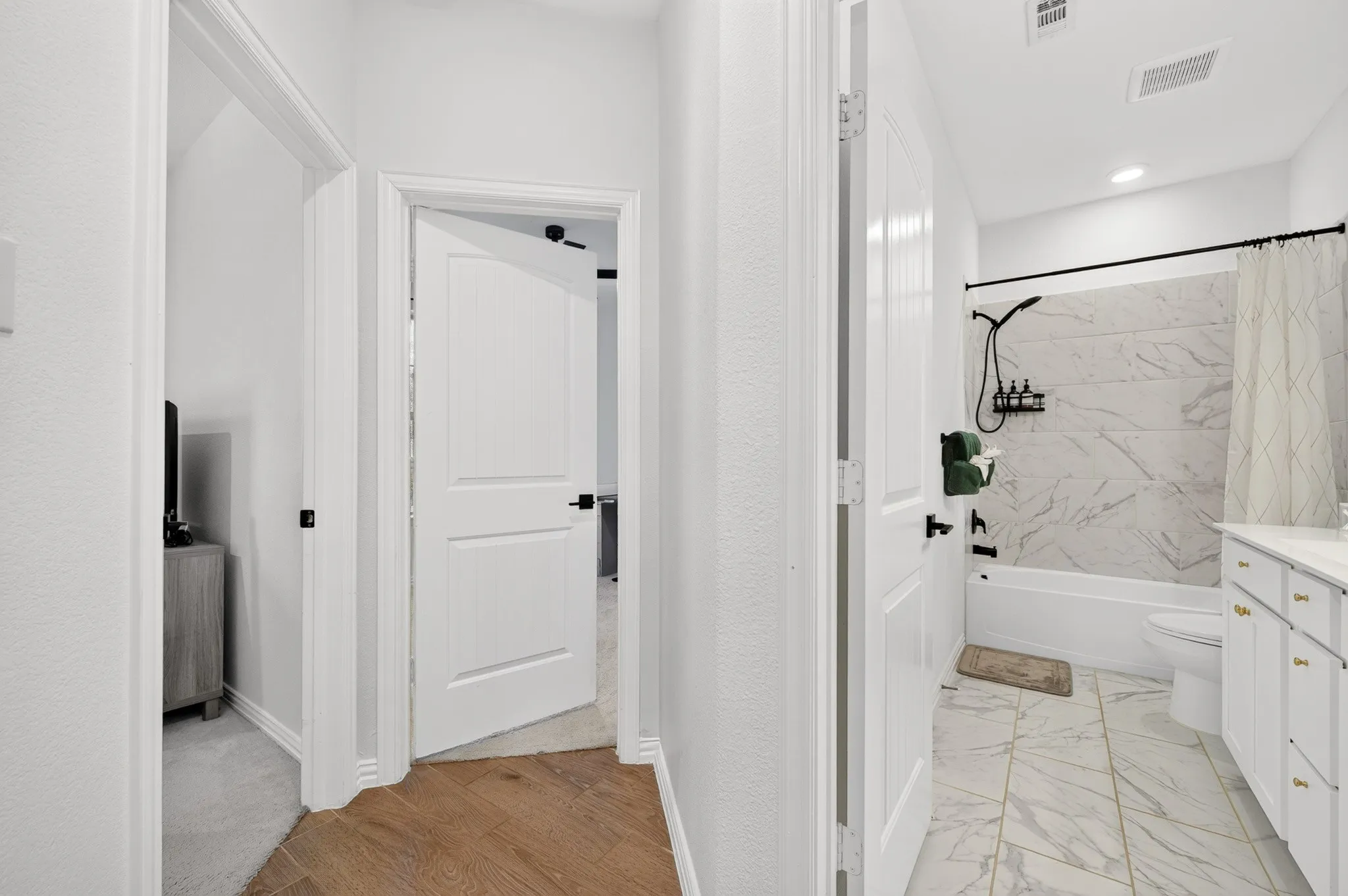 Primary bathroom featuring dual vanity with white cabinetry, marble-look tile backsplash, and matte black hardware